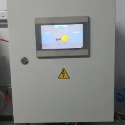 Szara szafa sterownicza z panelem dotykowym Weintek wyświetlającym schemat stacji z dwoma studniami, żółty znak ostrzegawczy z symbolem błyskawicy