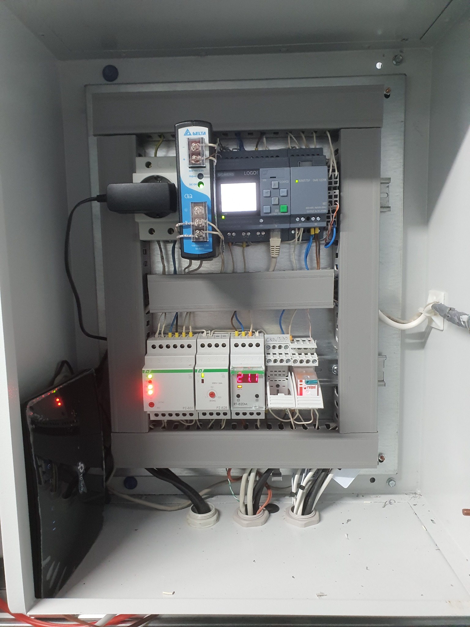 Szara szafa sterownicza z zamontowanym modułem Siemens LOGO!, zasilaczem Delta CliQ, oraz innymi elementami automatyki, widoczne przewody i listwy zaciskowe
