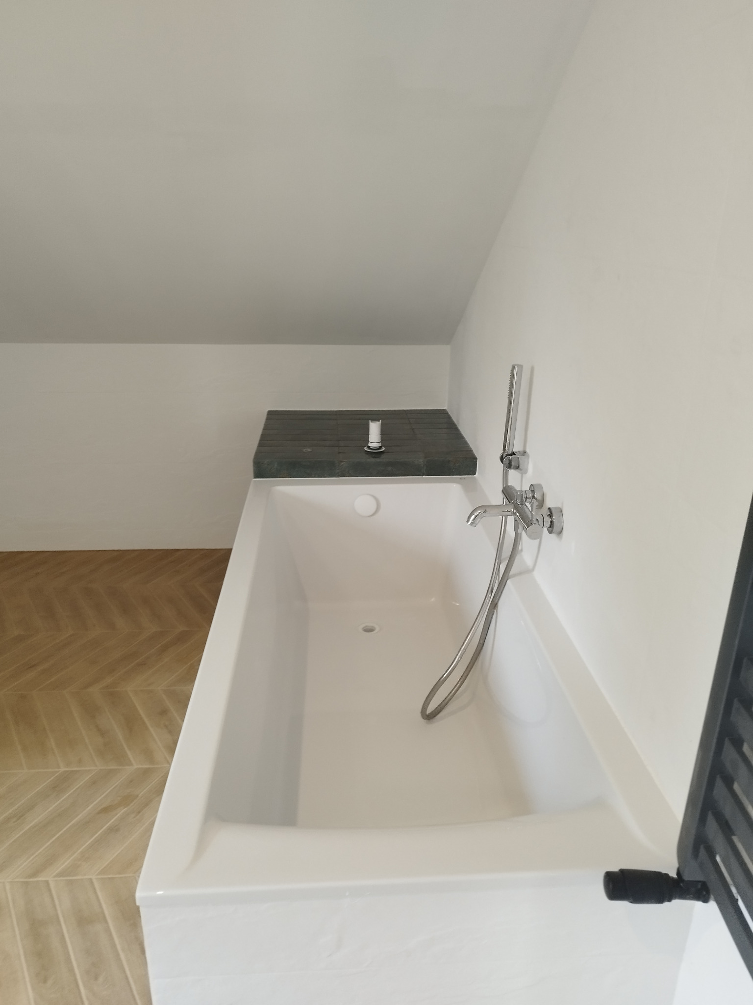 Nowoczesna biała wanna z chromowaną armaturą w łazience na poddaszu w Zamościu, z drewnianą podłogą ułożoną w jodełkę.