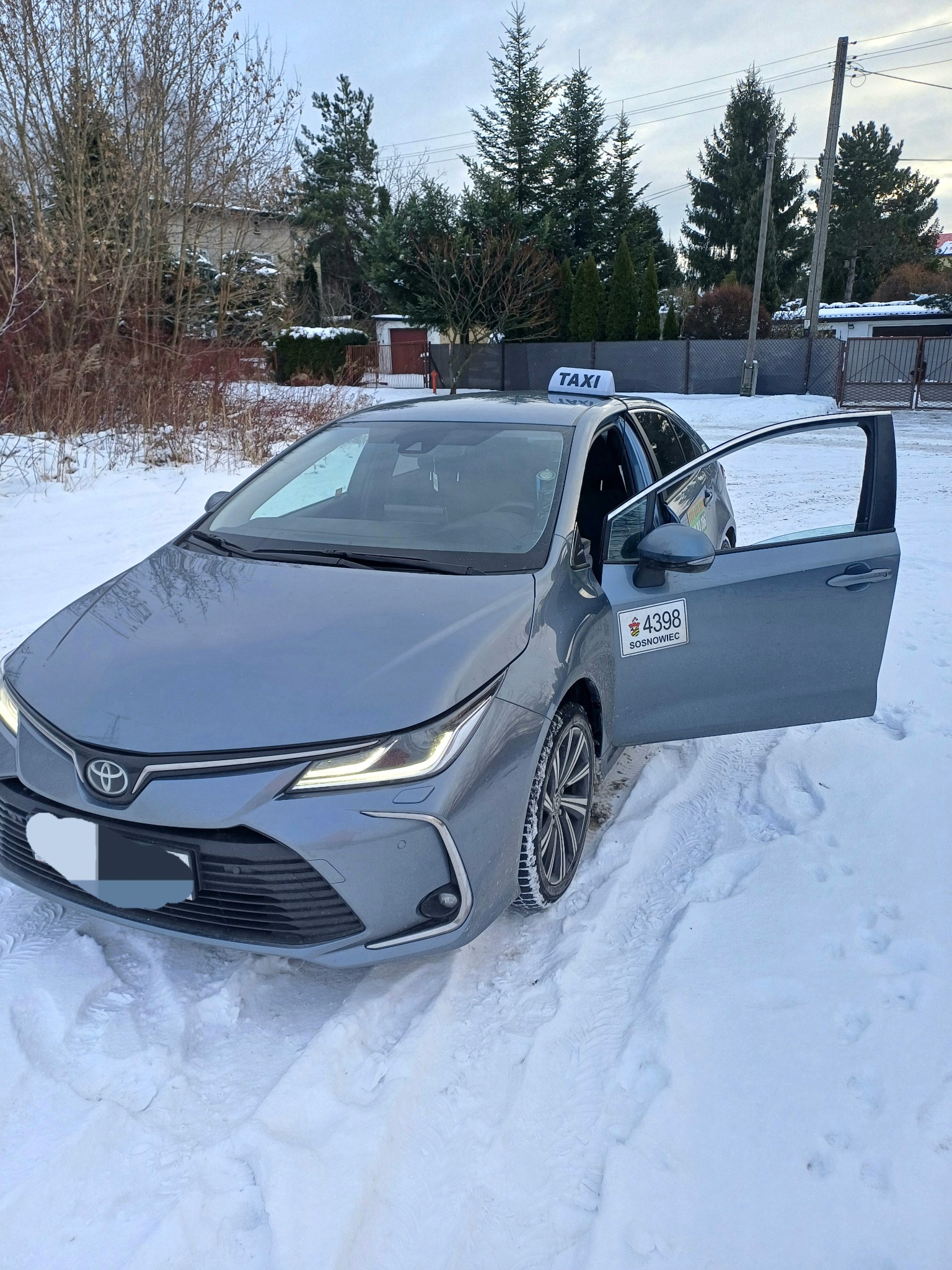Szary samochód osobowy z otwartymi drzwiami w zimowej scenerii, oznaczony jako taksówka z numerem bocznym 4398 Sosnowiec.