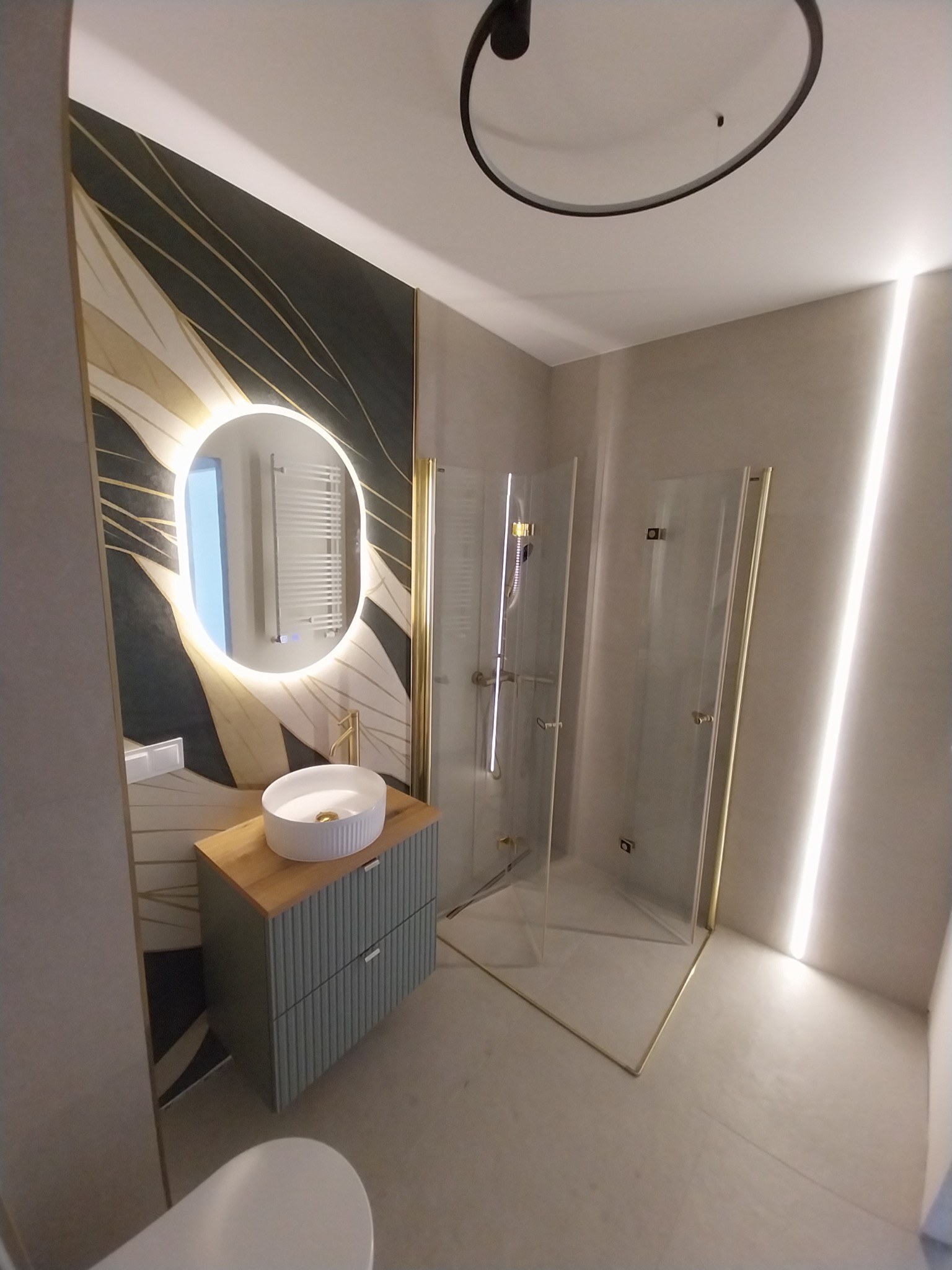 Nowoczesna łazienka z kabiną prysznicową, umywalką nablatową i podświetlanym lustrem. Dekoracyjna tapeta z motywem liści i subtelne oświetlenie LED.