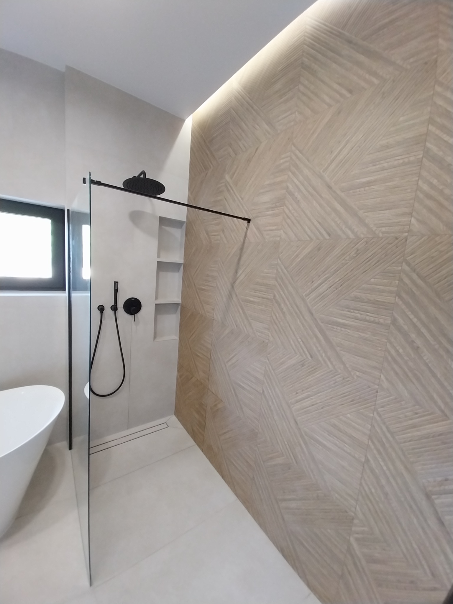 Nowoczesna łazienka z kabiną typu walk-in, czarną armaturą i ścianą wyłożoną dekoracyjną, drewnopodobną płytką w geometryczny wzór. Minimalistyczny design.