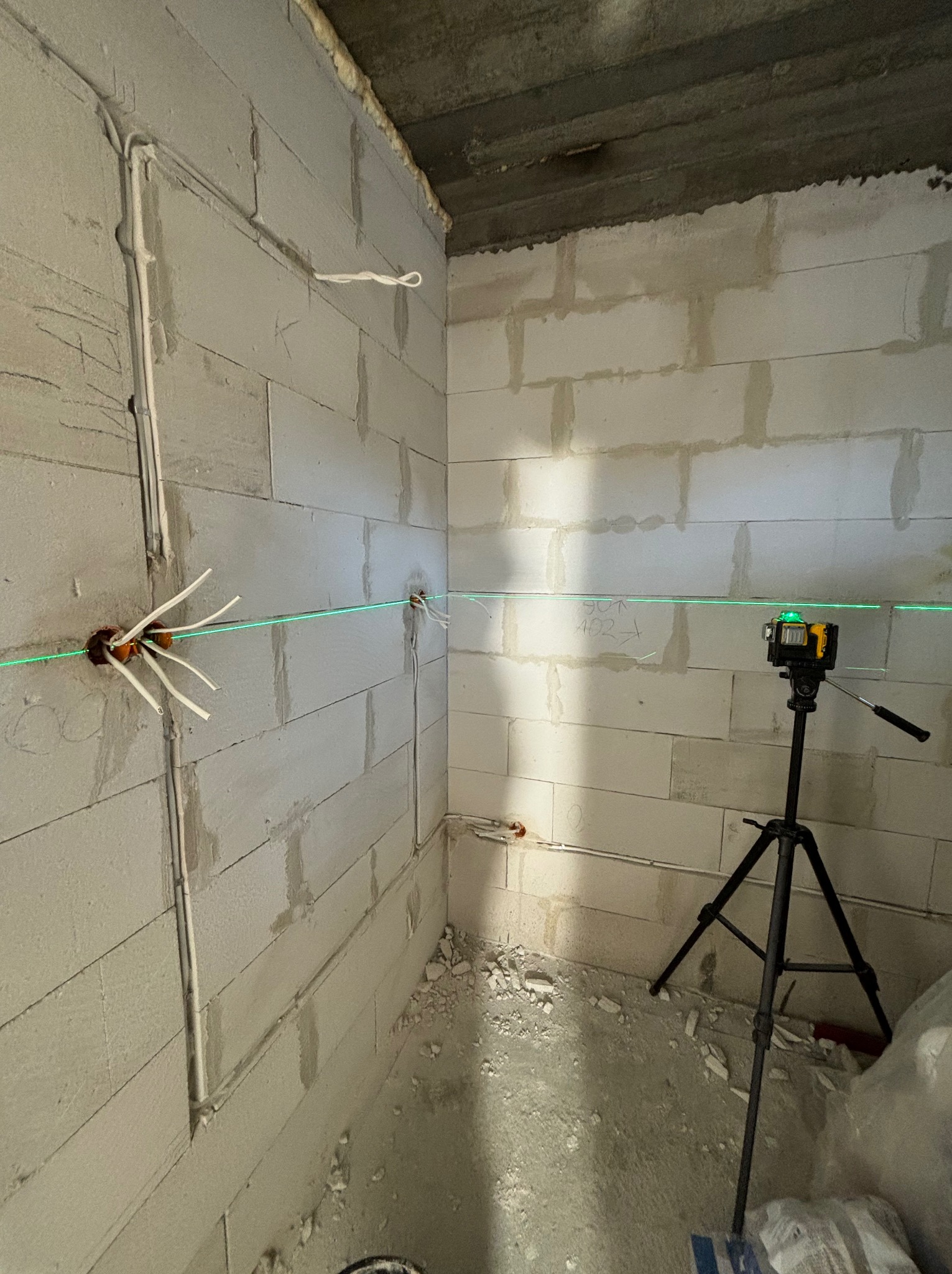 Surowy stan wnętrza z pustaków, widoczne przewody elektryczne wychodzące ze ścian, wyznaczanie poziomu laserem krzyżowym ustawionym na statywie.