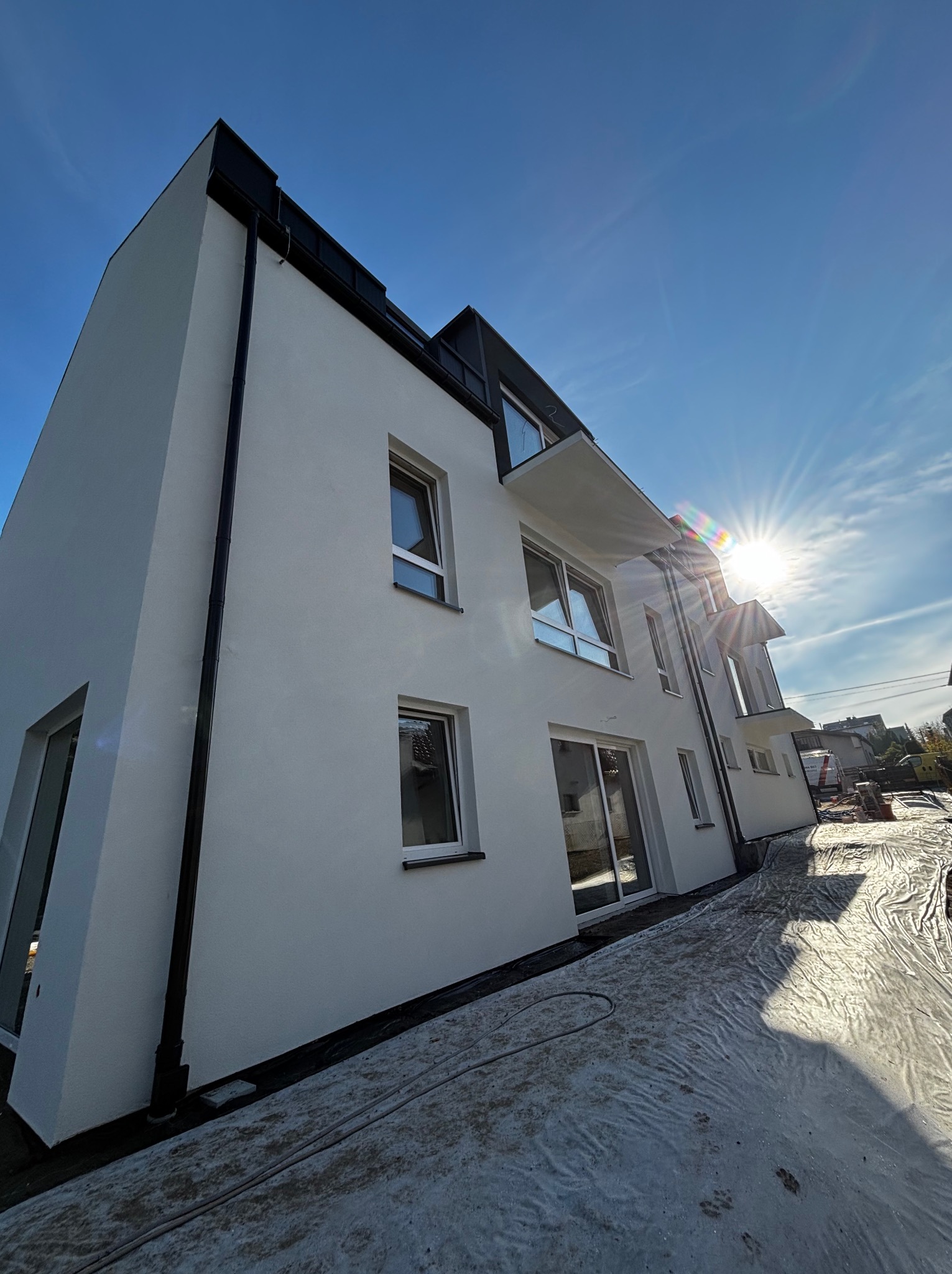 Nowo otynkowany, biały budynek w Bielsko-Białej, widoczny z dołu pod ostrym kątem, z zabezpieczonym folią terenem wokół, w silnym słońcu.