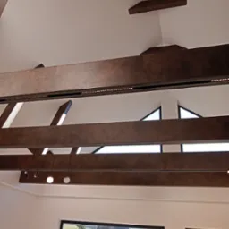 Nowoczesny sufit z drewnianymi belkami i wbudowanym oświetleniem LED, widok z dołu na tle okien z widokiem na wiejski krajobraz.