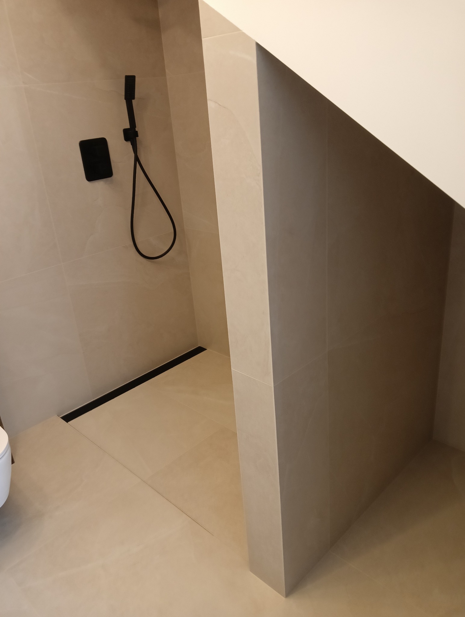 Nowoczesna kabina prysznicowa walk-in z czarną armaturą i odpływem liniowym w Wawrzeńczycach. Jasne płytki imitujące kamień. Minimalistyczny design.