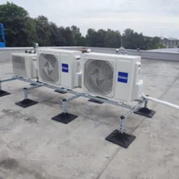 Instalacja kilku jednostek zewnętrznych klimatyzacji Haier i Fujitsu na płaskim dachu, widoczny niebieski podnośnik koszowy w oddali.
