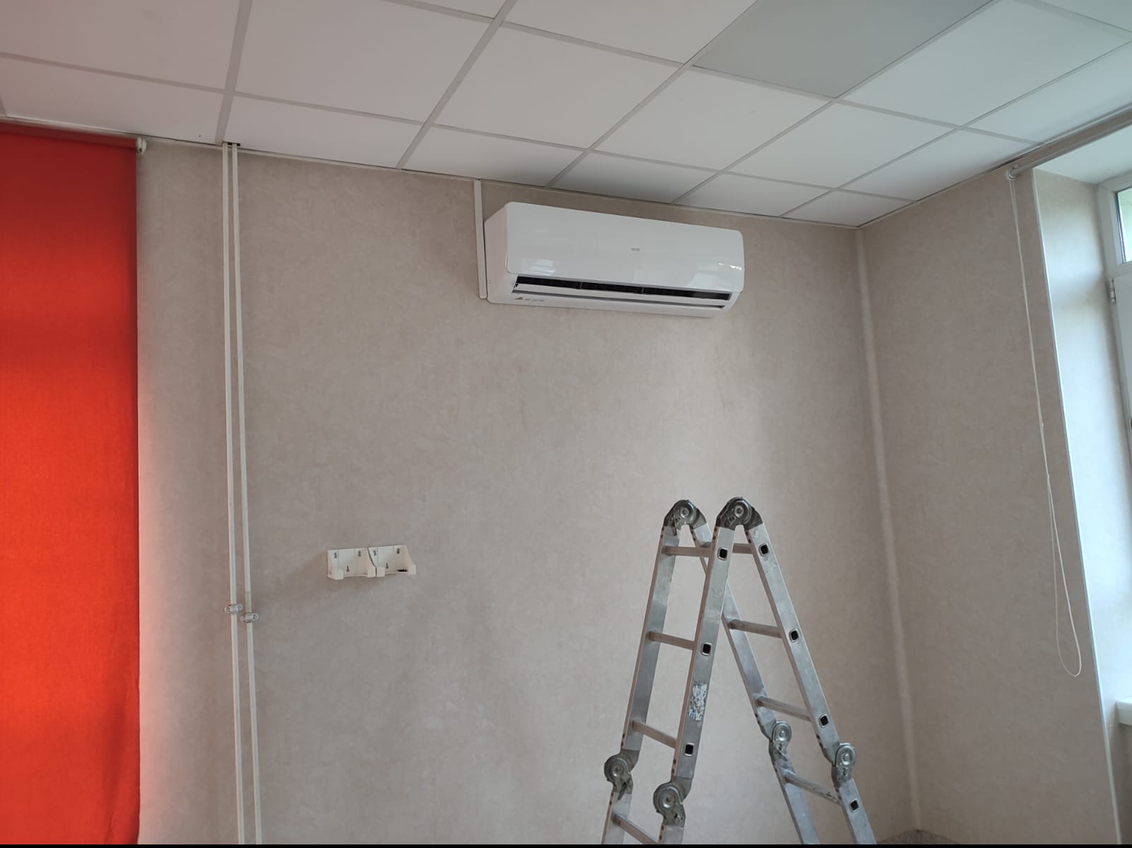 Biały klimatyzator ścienny zamontowany w pomieszczeniu w Łodzi, z widoczną drabinką aluminiową sugerującą trwający montaż lub serwis.