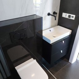 Paweł Spiączka - Nowoczesna łazienka w czarno-białej kolorystyce: wisząca toaleta z czarną spłuczką Geberit, umywalka nablatowa na czarnej szafce z chromowanymi uchwytami, czarna bateria ścienna i marmurowe płytki...