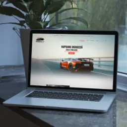 Laptop prezentujący stronę internetową firmy Wgniecenia-BP z Białej Podlaskiej, specjalizującej się w naprawie wgnieceń bez konieczności lakierowania. Na ekranie widoczny pomarańczowy samochód...