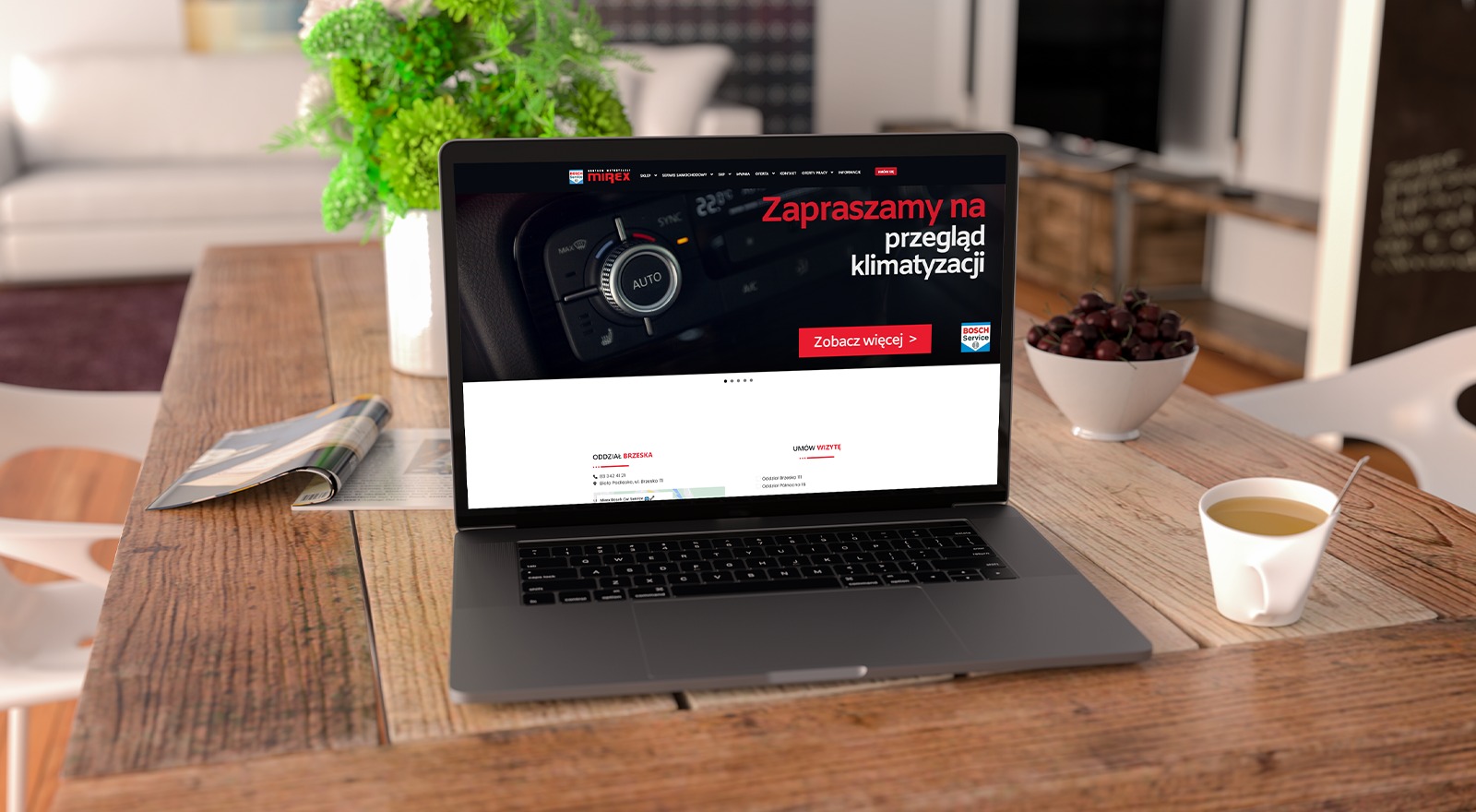 Laptop wyświetla stronę internetową firmy Mirex z zaproszeniem na przegląd klimatyzacji. Na drewnianym stole, obok laptopa, stoi filiżanka z napojem, miska z wiśniami, gazeta i wazon z kwiatami.
