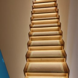 Piotr Jurczenko - Drewniane schody z podświetleniem LED na każdym stopniu, zabezpieczone taśmą malarską podczas prac wykończeniowych.