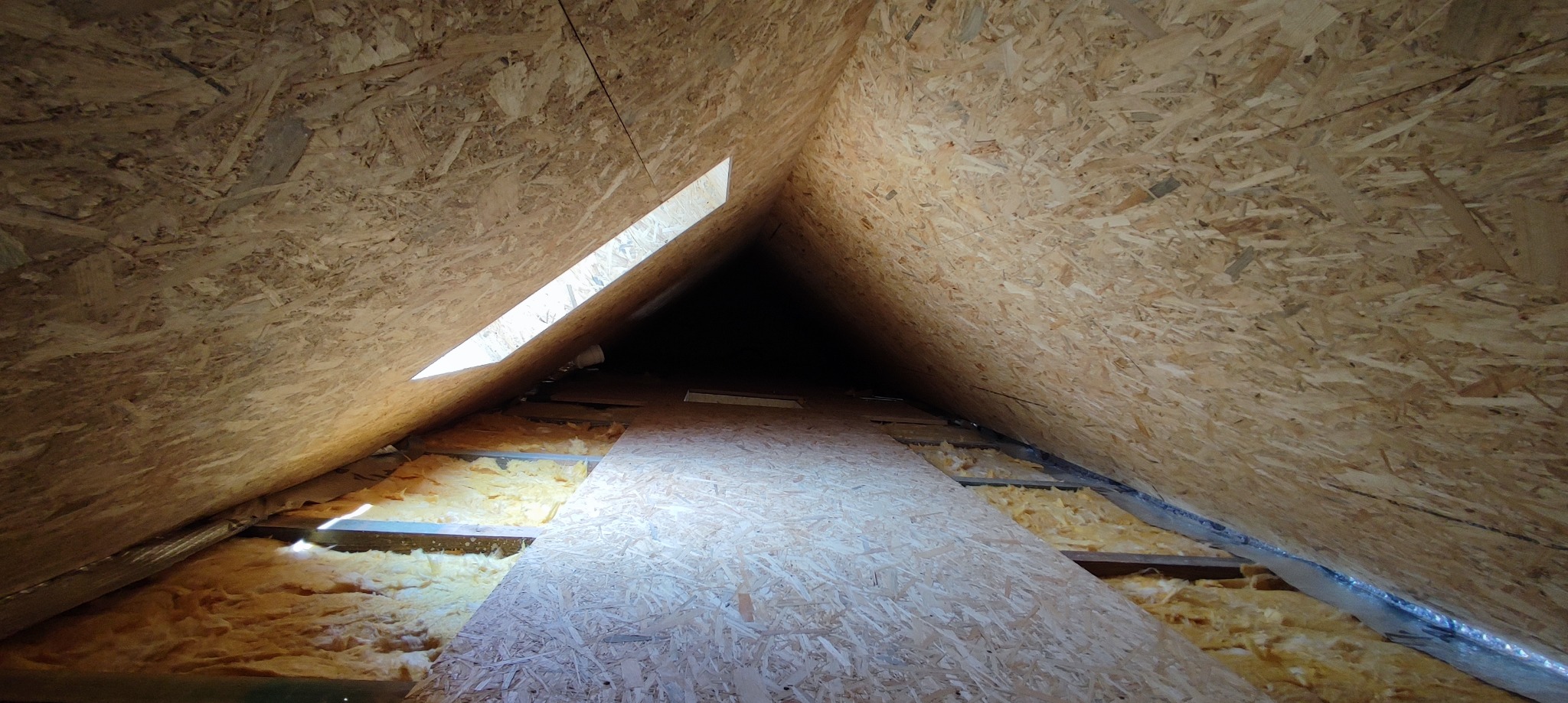 Ocieplenie poddasza wełną mineralną i wykończenie płytami OSB, widoczny fragment okna dachowego.