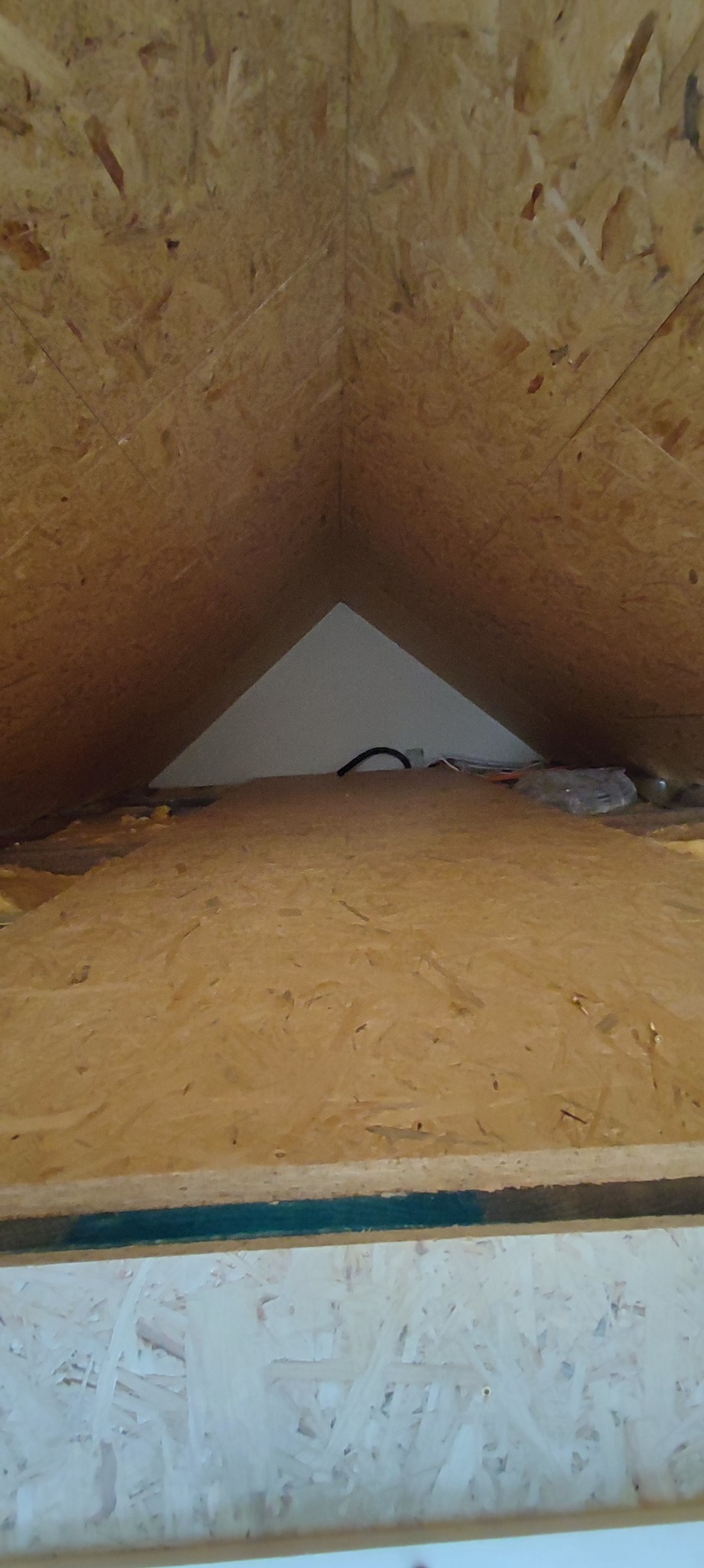 Skośny strych wykończony płytami OSB, widoczne kable i izolacja, surowe wykończenie poddasza.