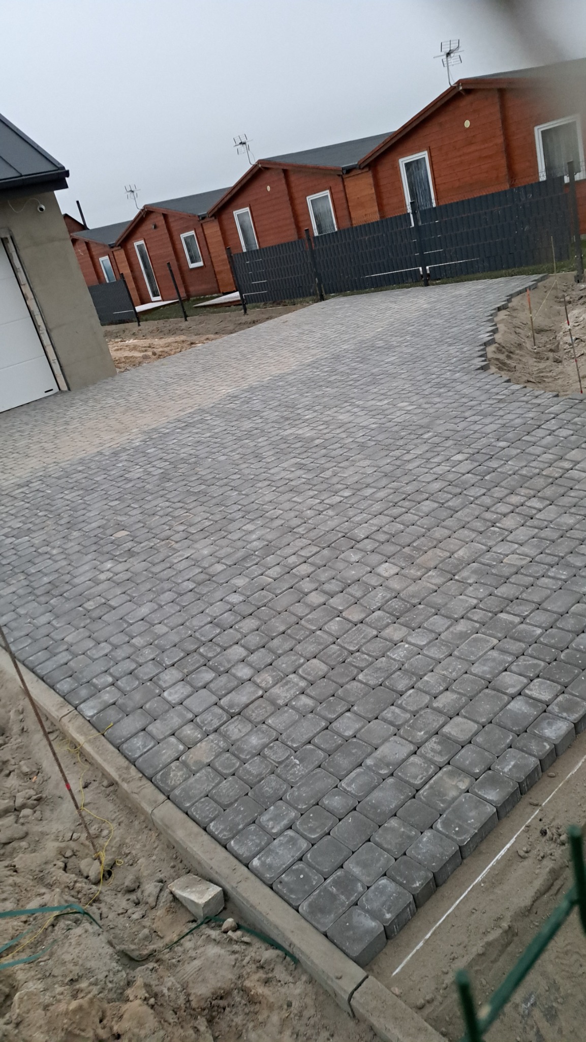Szara kostka brukowa ułożona na podjeździe do domków jednorodzinnych, widoczne obrzeża i przygotowane podłoże.