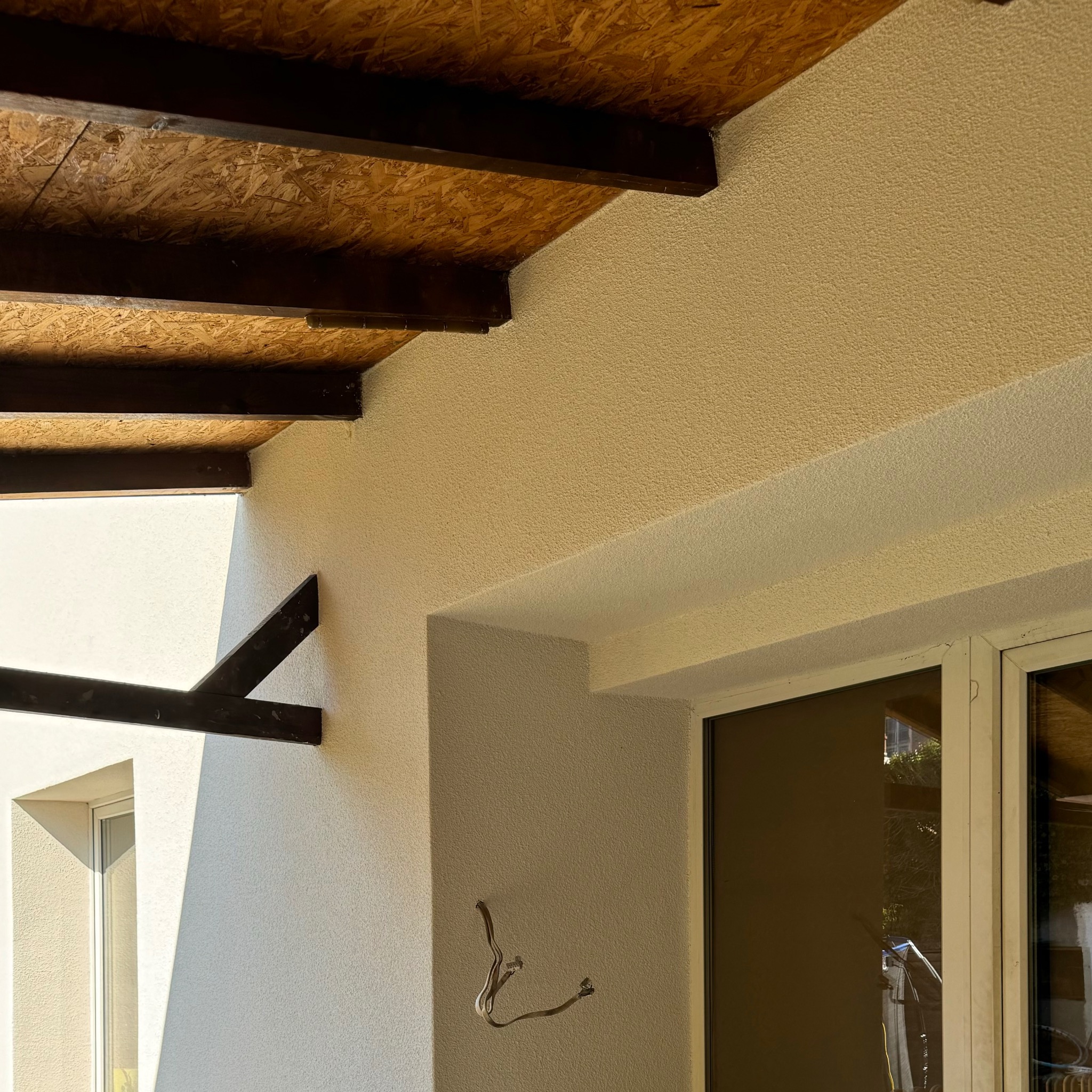 Fragment elewacji budynku z wyprowadzonymi przewodami elektrycznymi, widoczne okno i drewniana konstrukcja dachu.