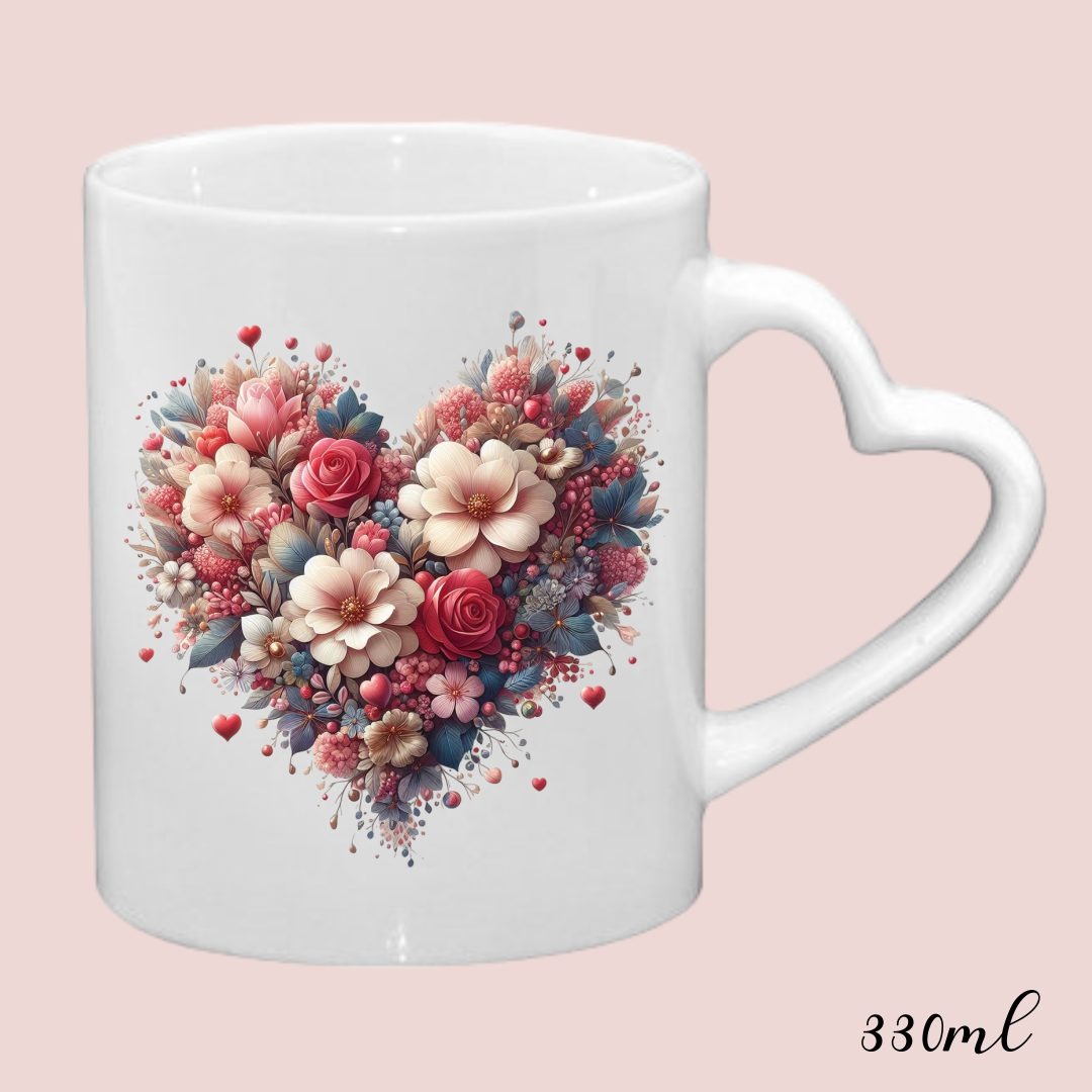 Biały kubek z uchwytem w kształcie serca, ozdobiony kwiatowym wzorem w kształcie serca z różami i innymi kwiatami w odcieniach różu, bieli i niebieskiego, na jasnoróżowym tle.