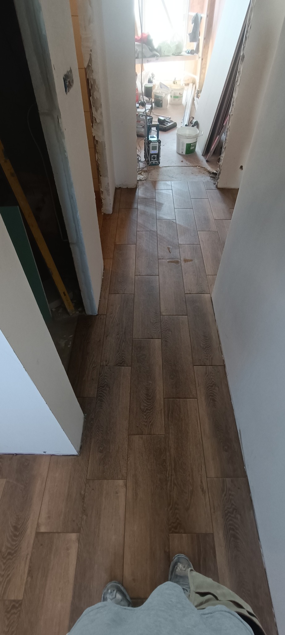 Ułożone brązowe panele podłogowe imitujące drewno w korytarzu podczas prac wykończeniowych, widoczne narzędzia i materiały budowlane w tle.