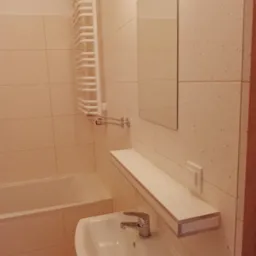 Jasna łazienka po remoncie, widoczna umywalka z baterią, lustro, grzejnik drabinkowy oraz płytki na ścianach.