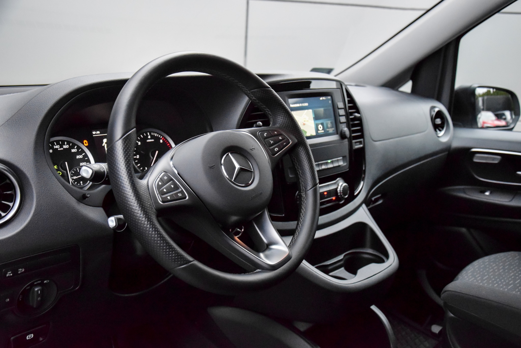 Wnętrze samochodu Mercedes Vito z widoczną deską rozdzielczą, kierownicą z logo, nawigacją i zegarami. Czarna tapicerka i srebrne akcenty na kierownicy.