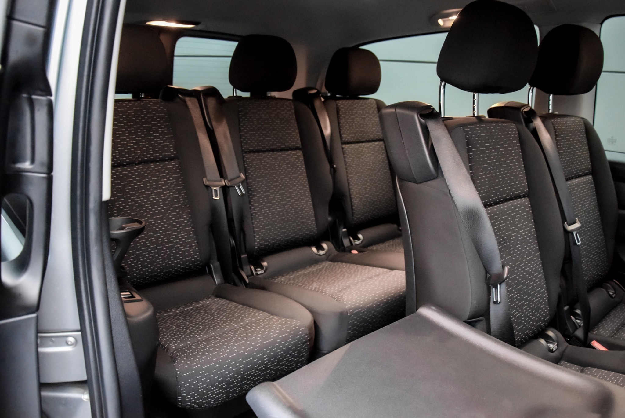 Wnętrze busa z trzema rzędami foteli z ciemną tapicerką w drobny wzór, widoczne pasy bezpieczeństwa i zagłówki.