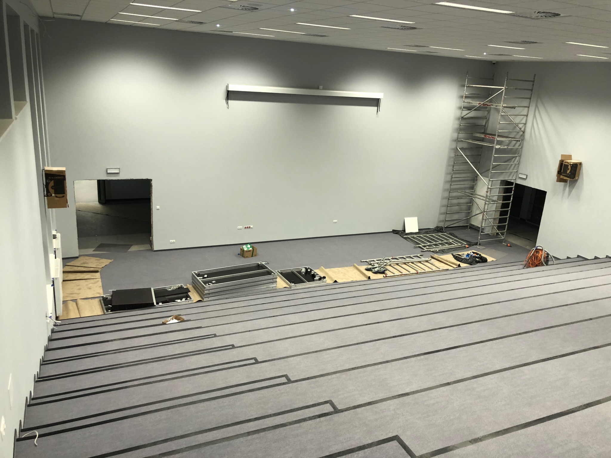 Duże pomieszczenie biurowe w trakcie prac wykończeniowych; widoczne rusztowanie, elementy konstrukcyjne, zabezpieczona podłoga i surowe ściany.