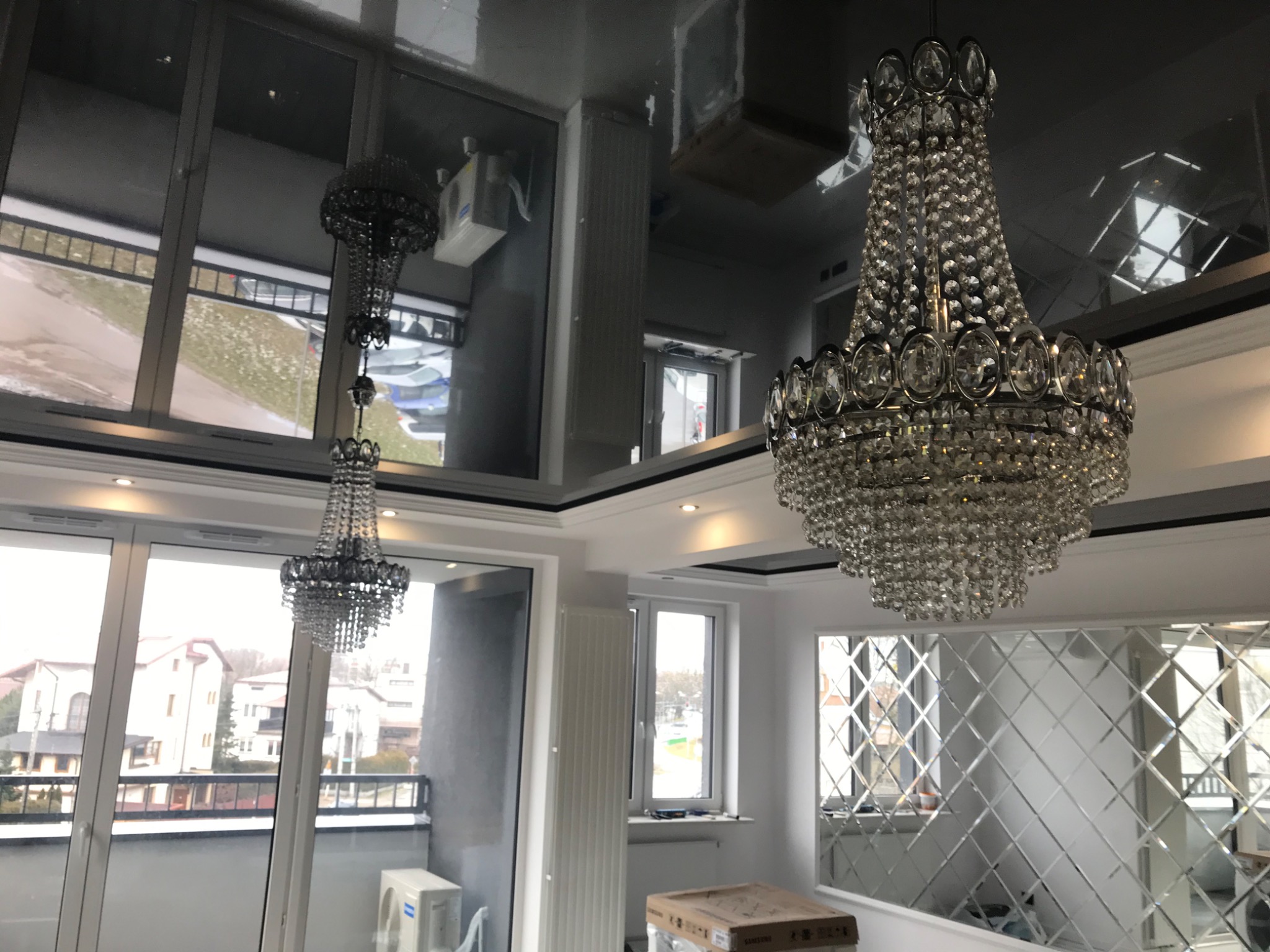 Kryształowy żyrandol w nowoczesnym wnętrzu z lustrzanym sufitem, widok na balkon i mozaikę lustrzaną na ścianie.