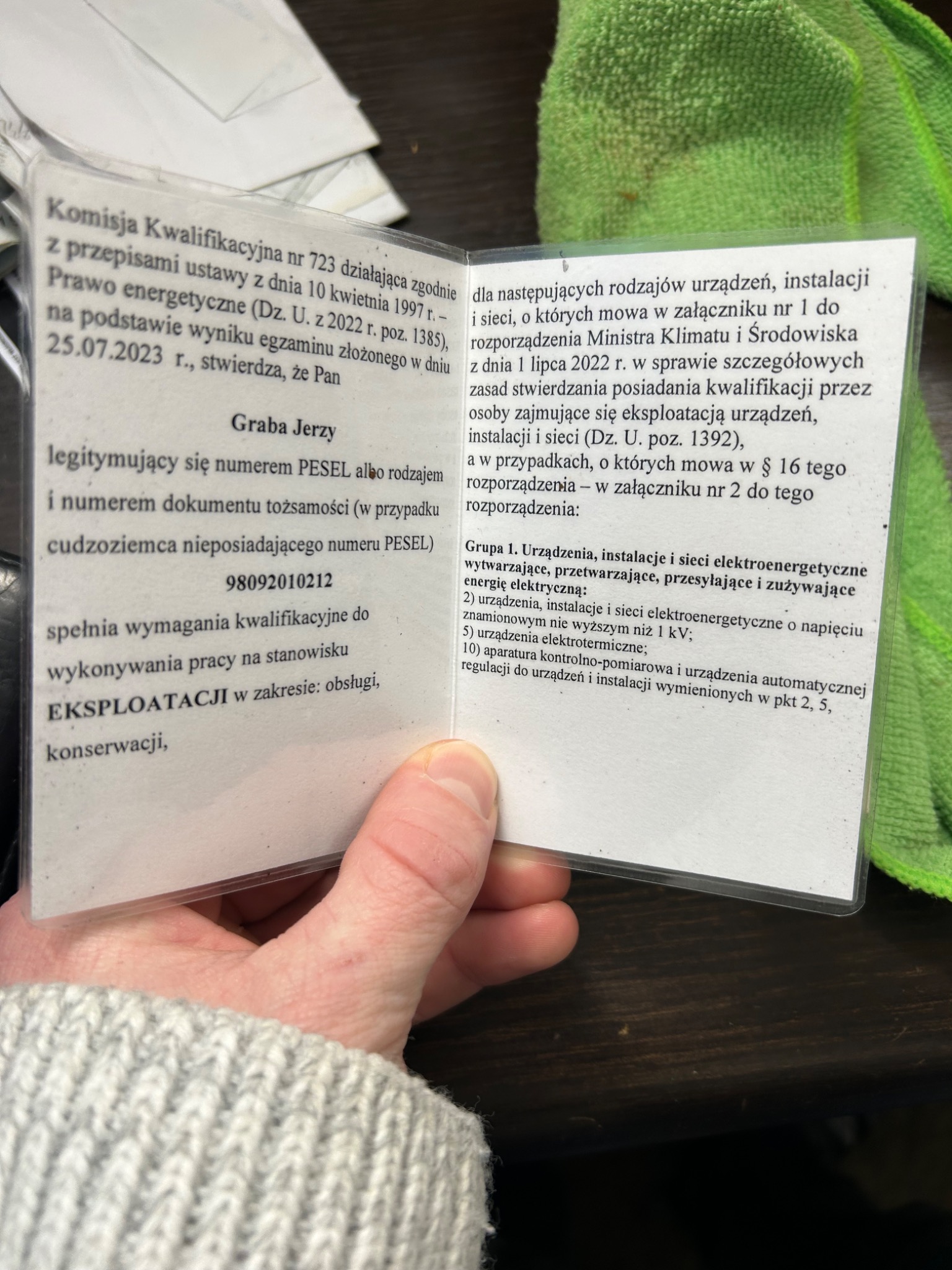 Świadectwo kwalifikacyjne Graba Jerzego do wykonywania pracy na stanowisku eksploatacji urządzeń, instalacji i sieci elektroenergetycznych, w plastikowej osłonie, trzymane w dłoni.