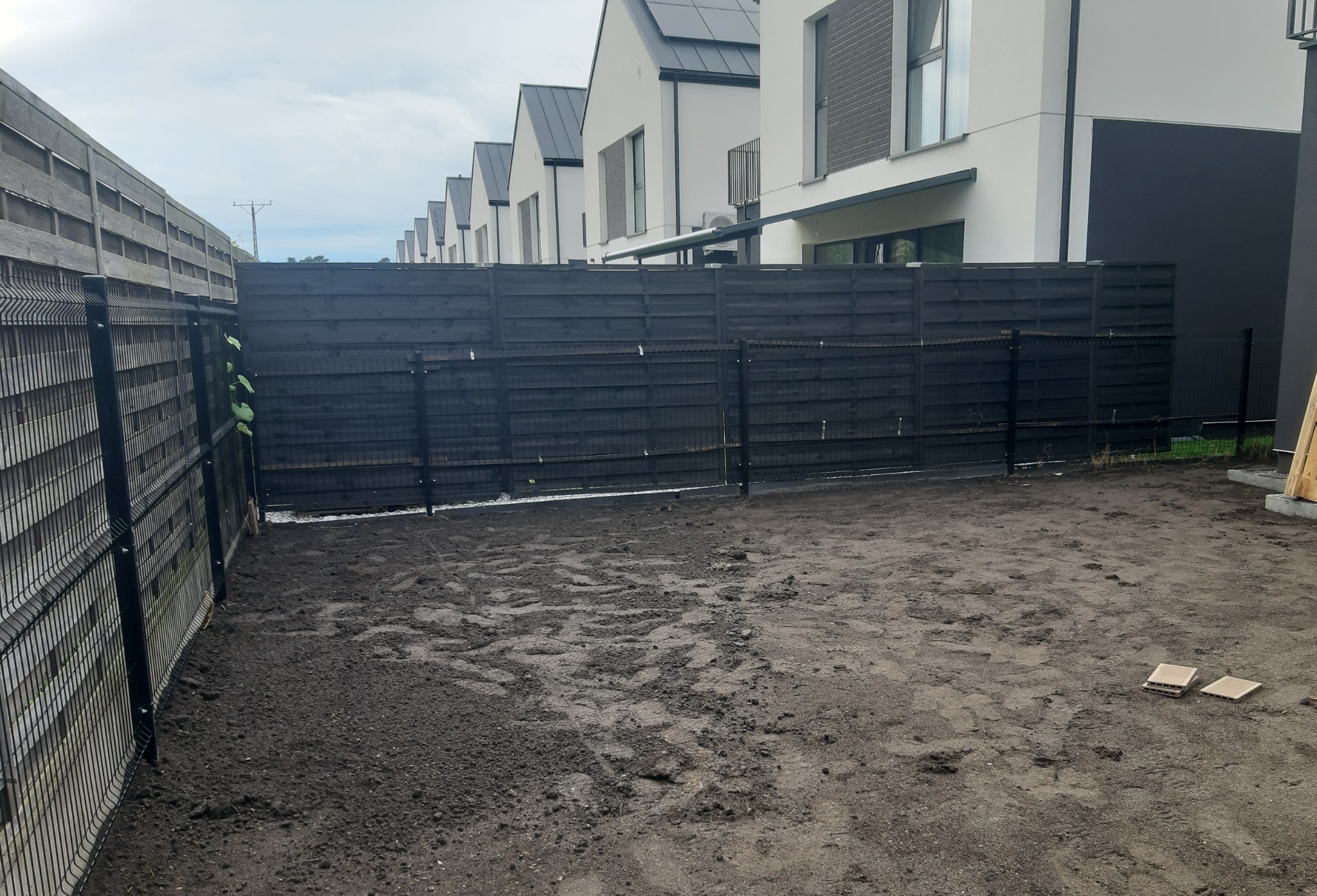 Przygotowany teren pod trawnik w Piasecznie, widoczne ślady po pracach ziemnych, ogrodzenie panelowe i drewniane, w tle nowoczesne domy.