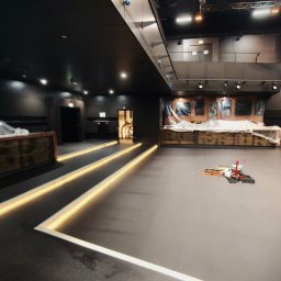 PAWEŁ GUNIA PAGAN - Ciemna, gładka posadzka z wbudowanym oświetleniem liniowym w lokalu usługowym. W tle bar zabezpieczony folią i narzędzia pracy.