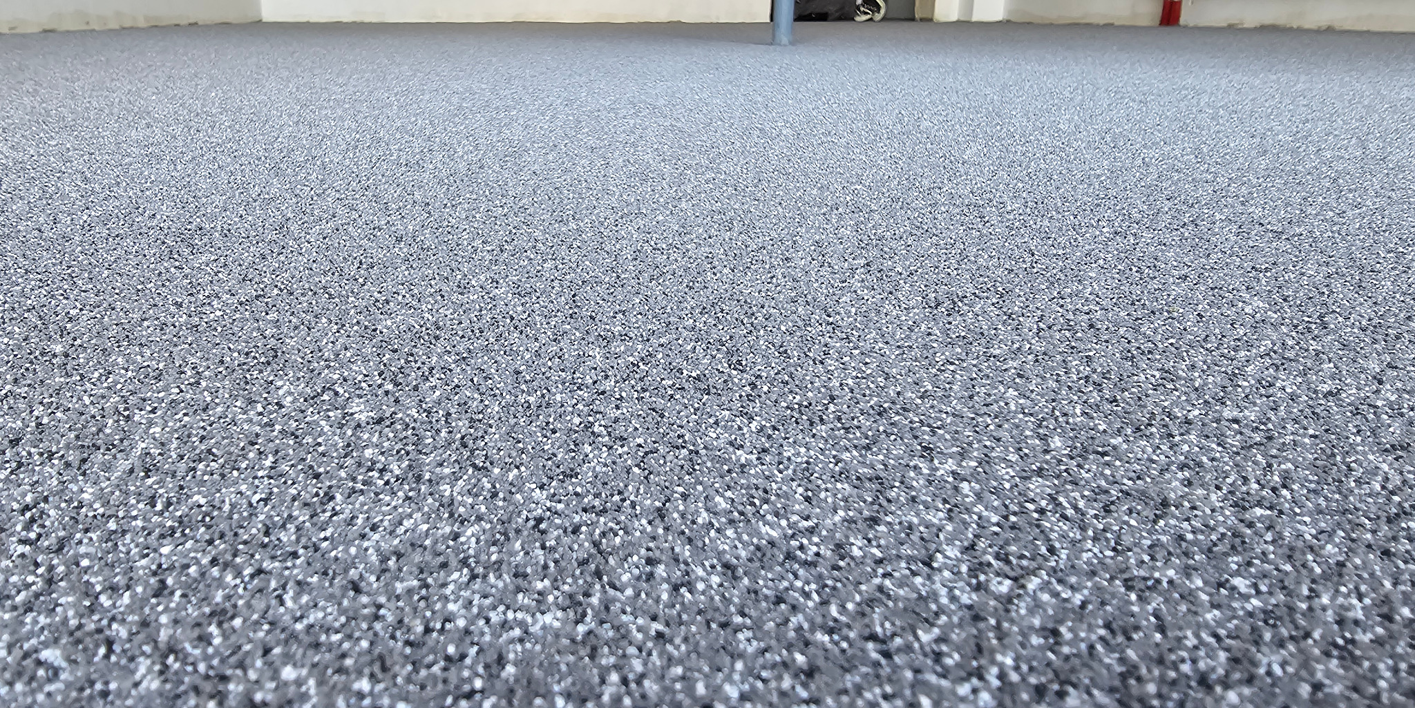 Szara, drobnoziarnista posadzka w jasnym pomieszczeniu, widok z niskiej perspektywy, podkreślający fakturę i równomierność wykonania. W tle widoczne elementy instalacji.