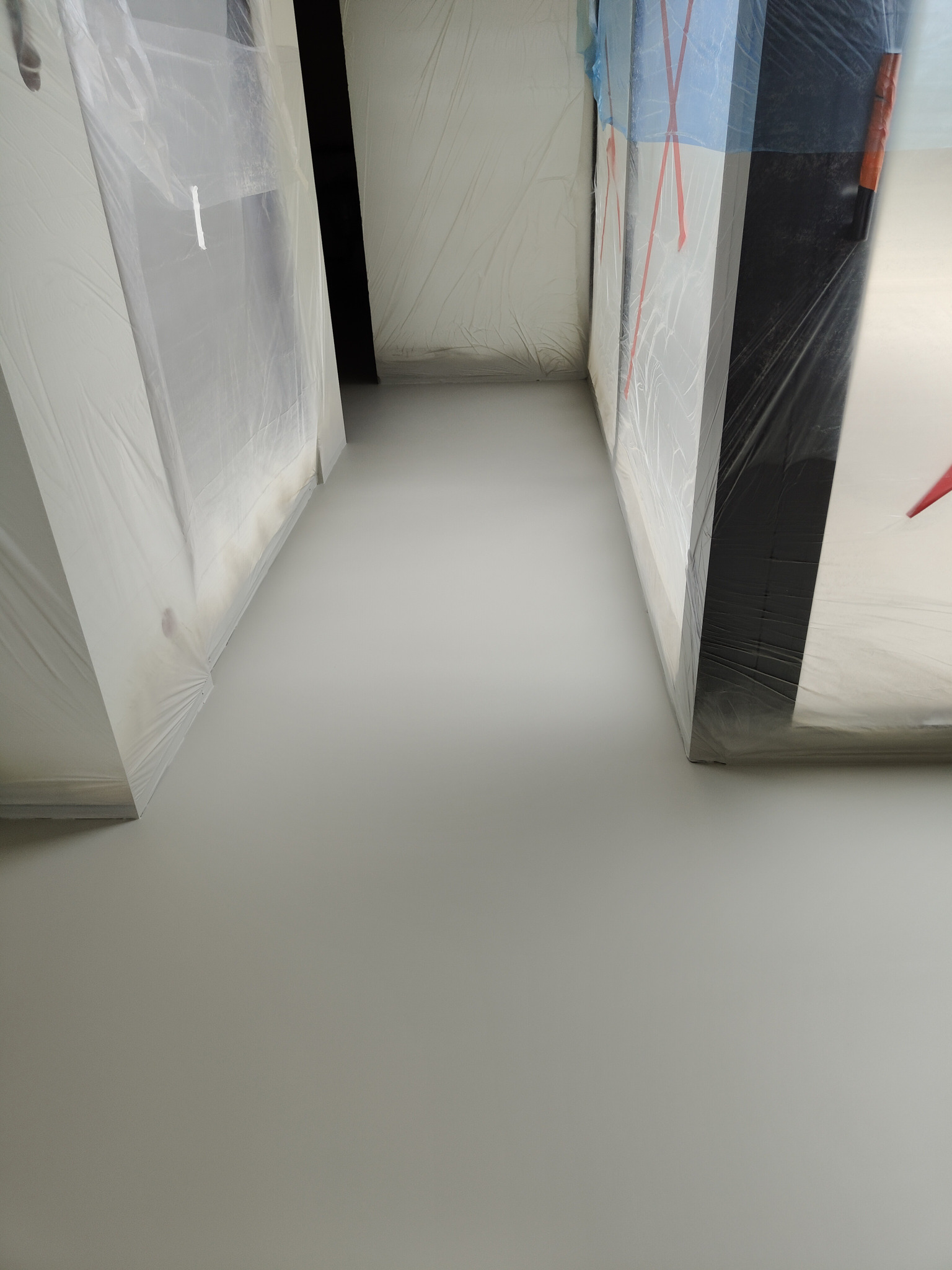 Świeżo wylana, jasnoszara posadzka żywiczna w pomieszczeniu z zabezpieczonymi folią malarską drzwiami i ścianami. Widok z dołu, perspektywa zbieżna.