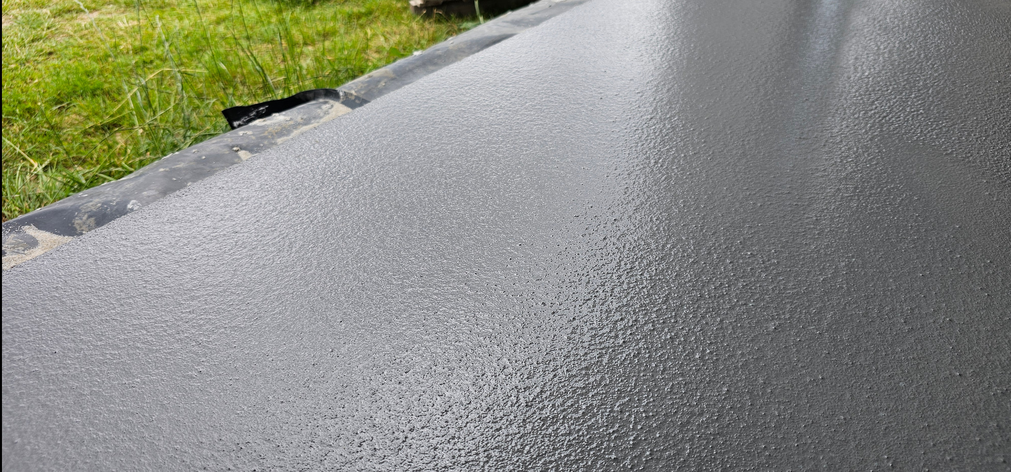 Świeżo wylana, szara posadzka żywiczna z widoczną strukturą i fragmentem zieleni w tle. Detal wykończenia powierzchni.