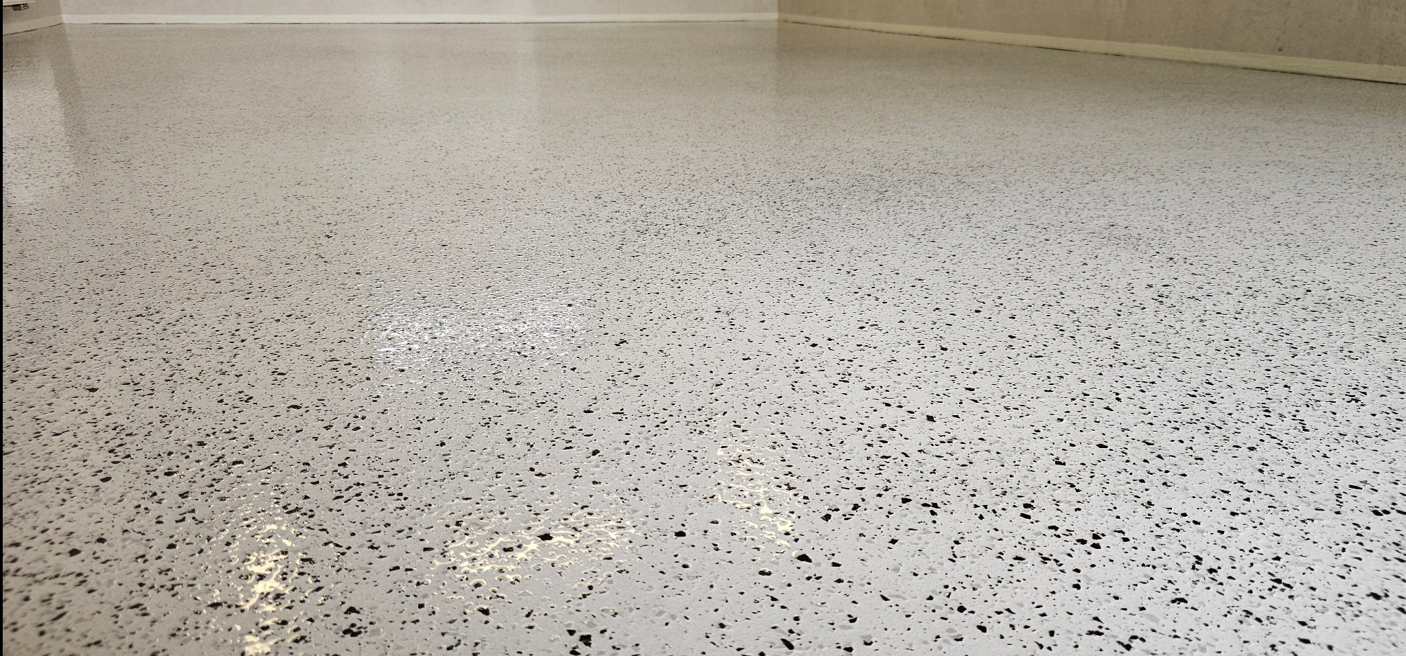 Jasna posadzka żywiczna z czarnymi drobinkami, gładka powierzchnia. Widok z niskiego kąta, ukazujący jednolitą strukturę i połysk wykończenia.