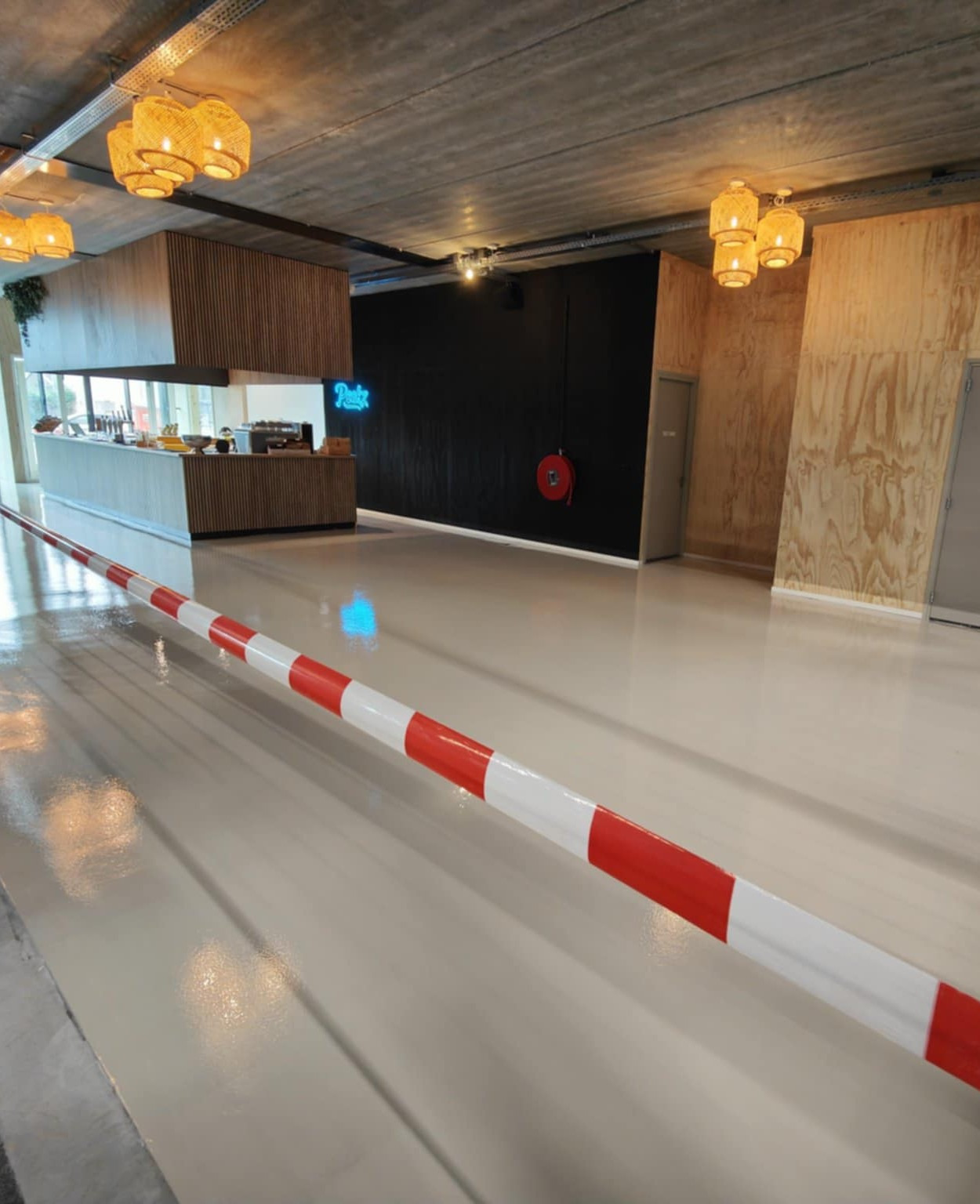 Jasna, błyszcząca posadzka w lokalu z drewnianymi elementami wykończenia i neonem. Barierka z biało-czerwonymi pasami na pierwszym planie.