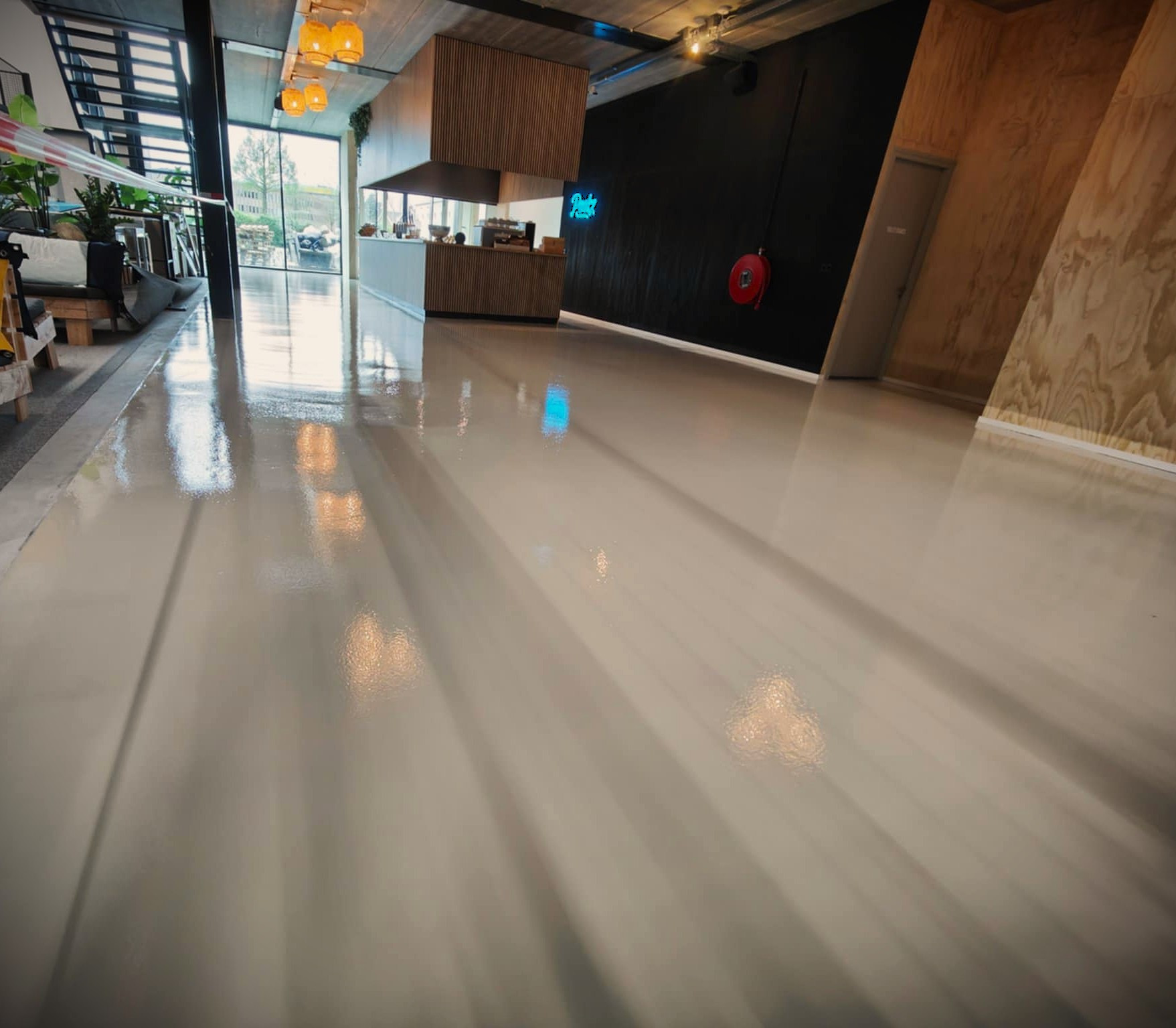 Jasna, błyszcząca posadzka w nowoczesnym wnętrzu kawiarni. Widoczne odbicia światła i elementy wystroju, takie jak bar i schody. Minimalistyczny design.