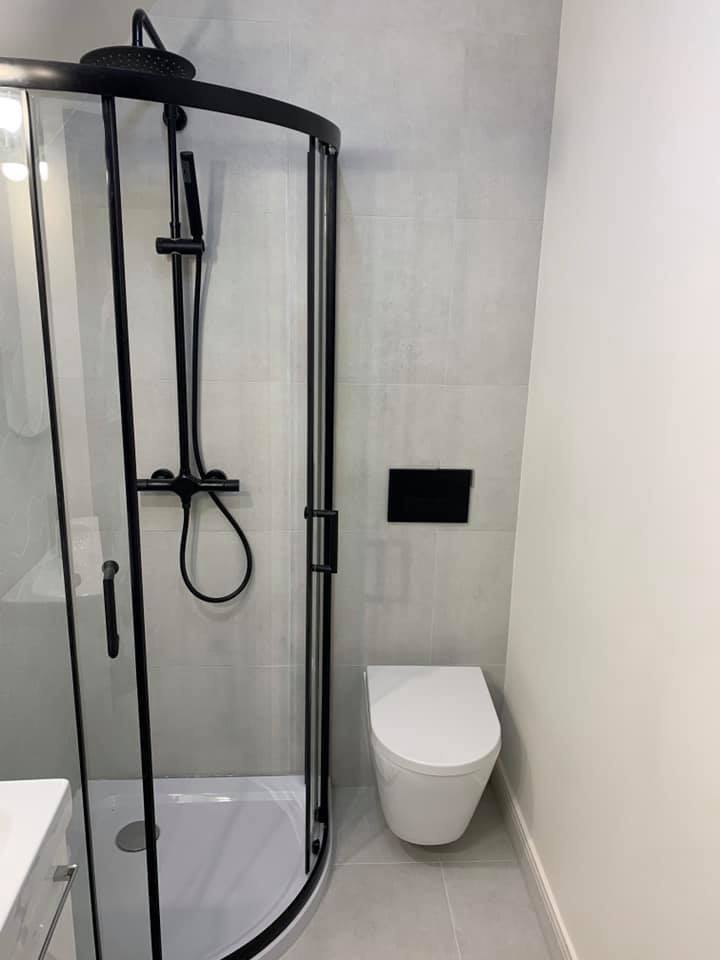 Nowoczesna łazienka z kabiną prysznicową z czarnymi profilami, wiszącą toaletą i szarymi płytkami.