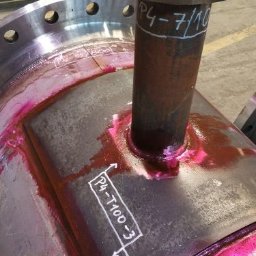 WELD-PROJECT - Spawanie rury do zbiornika z testem penetracyjnym w kolorze różowym. Widoczne białe oznaczenia na metalu. Fragment konstrukcji stalowej w hali.