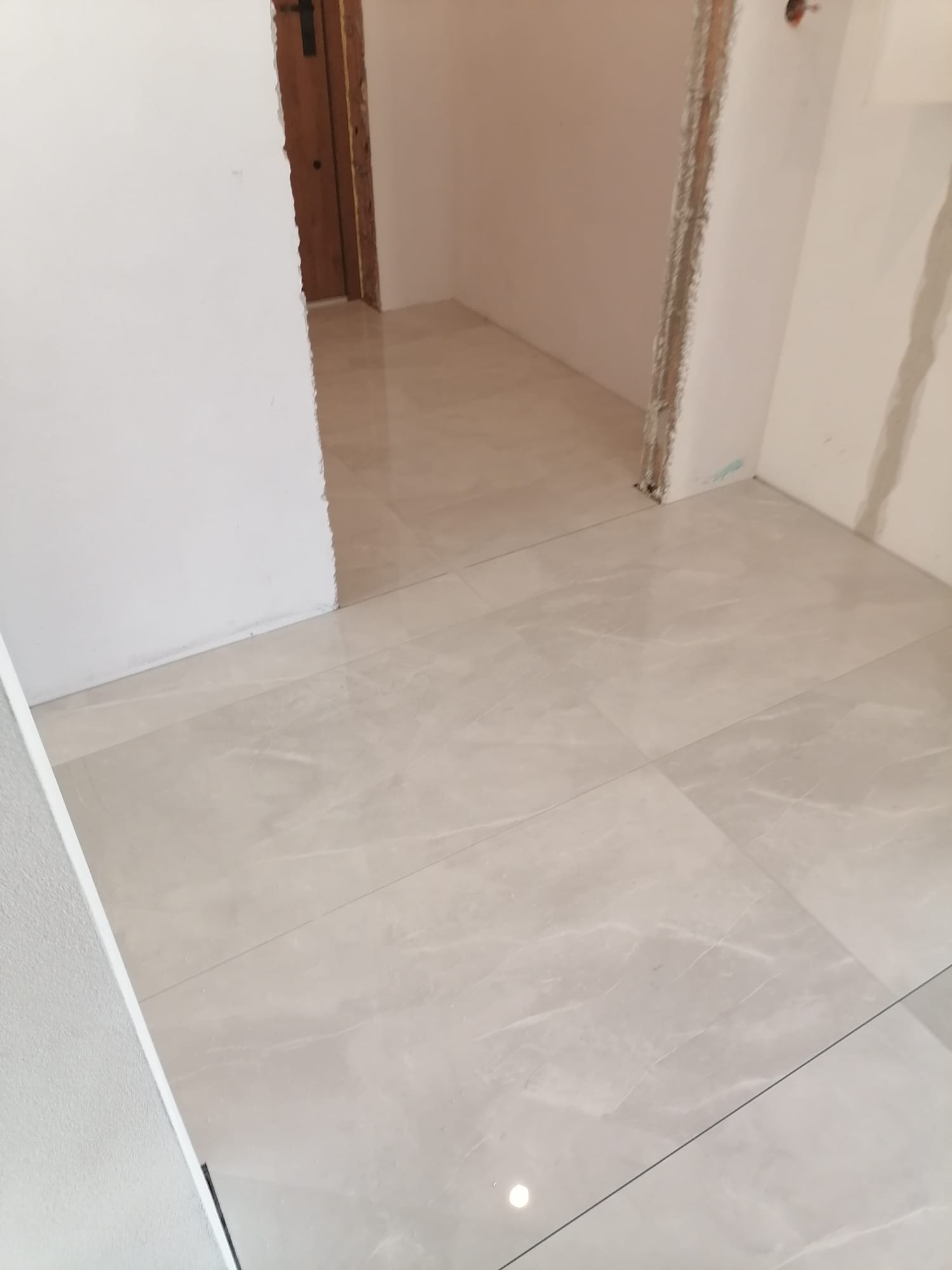 Ułożone jasne, marmurowe płytki podłogowe w nowym pomieszczeniu, widoczne surowe wykończenie ścian i ościeżnic.