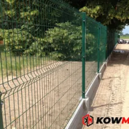 Zielone ogrodzenie panelowe z podmurówką betonową, widoczne z boku, z logo firmy w prawym dolnym rogu.