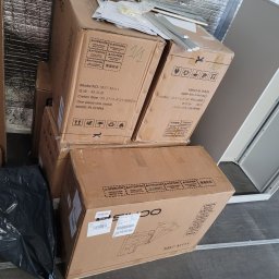 Krystian Kuna - Stos kartonów z modelem M57-M111, wiertarka akumulatorowa i metalowe profile leżące na wierzchu. Przygotowanie do montażu w pomieszczeniu z izolacją.