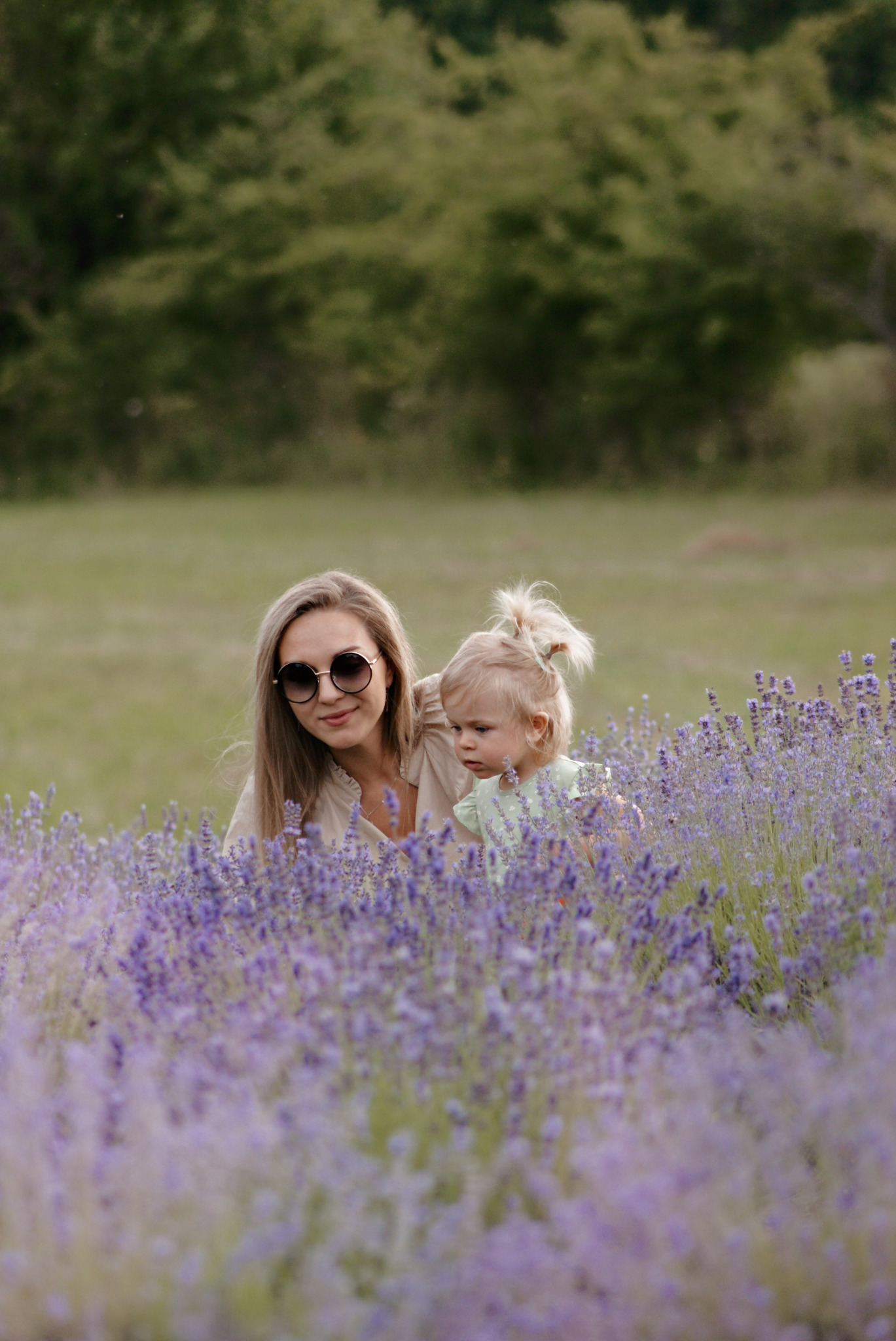 Matka w okularach przeciwsłonecznych trzyma córkę na tle pola lawendy.