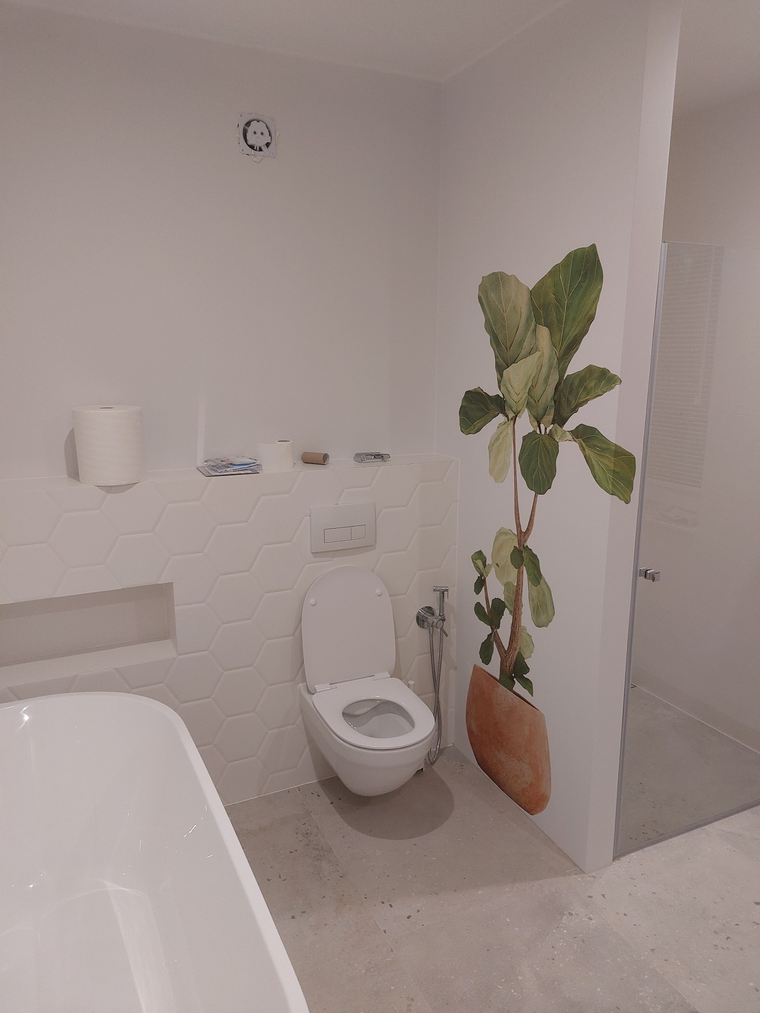 Biała łazienka z toaletą, wanną i dekoracyjną naklejką roślinną na ścianie obok kabiny prysznicowej.