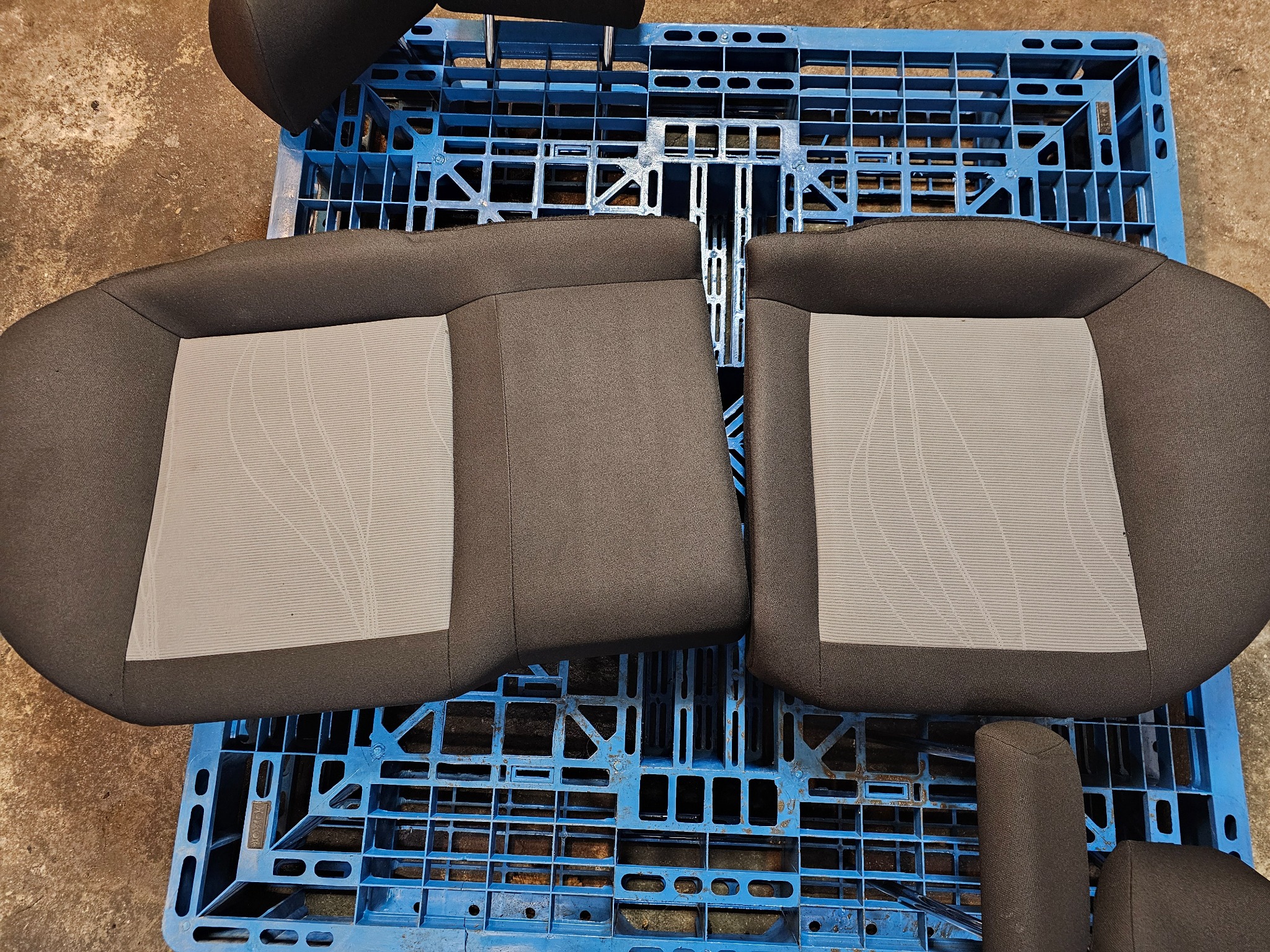 Dwa szare fotele samochodowe z jasnoszarymi wstawkami o geometrycznym wzorze, ułożone na niebieskiej plastikowej palecie.