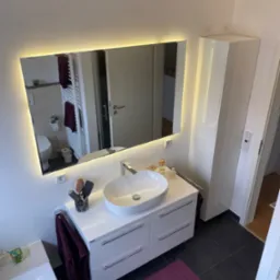 Nowoczesna łazienka z białą szafką pod umywalkę, podświetlanym lustrem i ciemną podłogą, widok z góry.