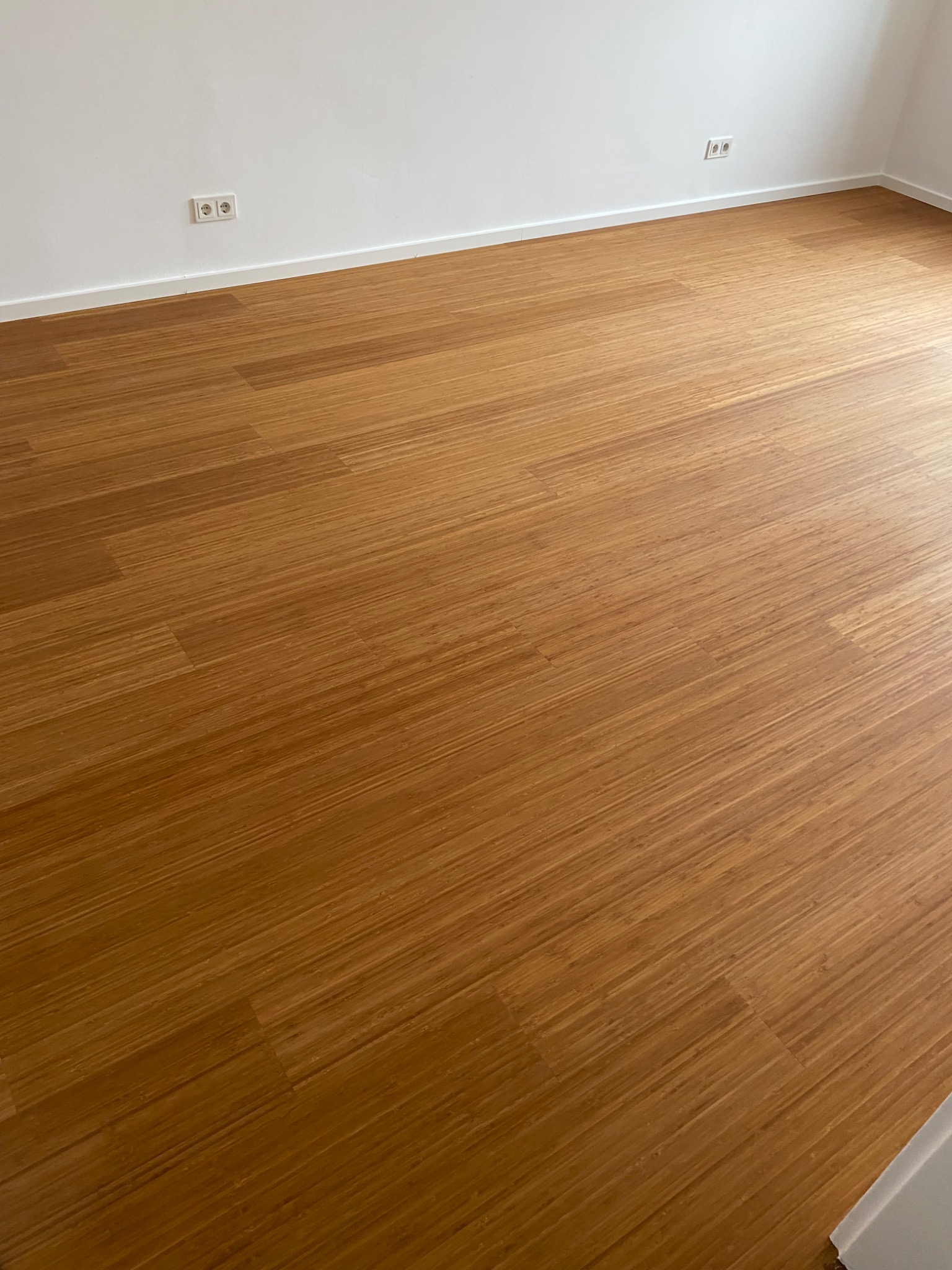 Ułożona, drewniana podłoga w pustym pokoju w Andrychowie, widoczne gniazdka elektryczne na białej ścianie.