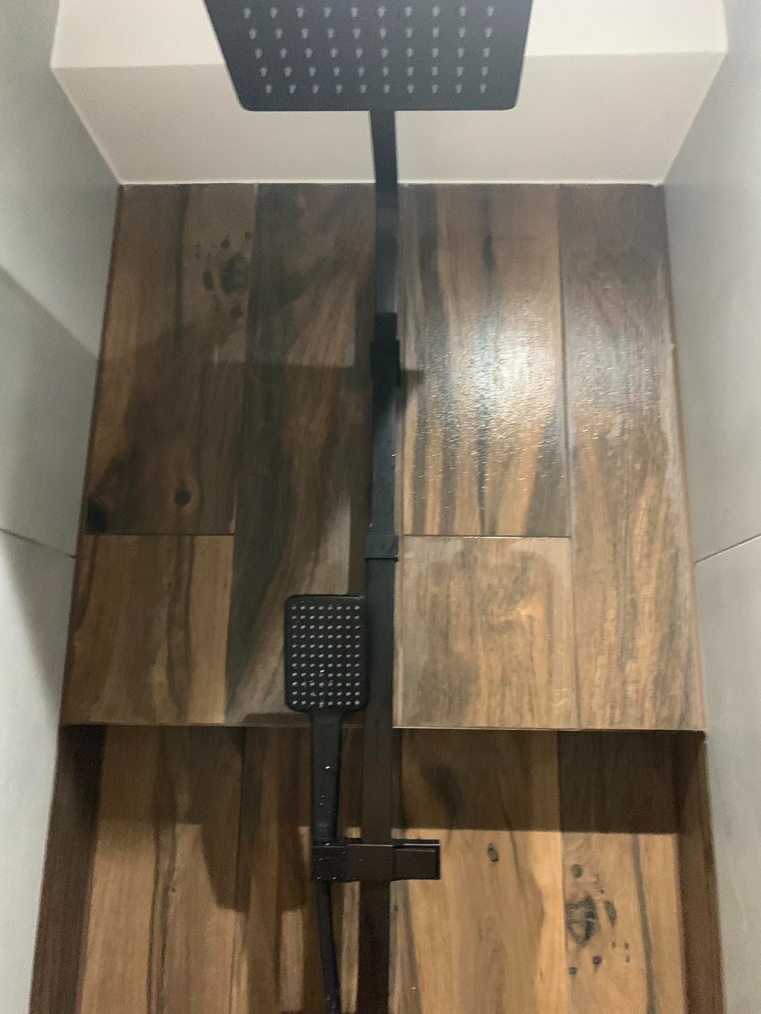 Nowoczesny prysznic z czarną armaturą i drewnopodobnymi płytkami w kabinie typu walk-in.