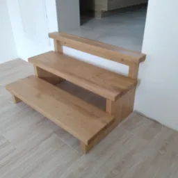 Krótkie, dwustopniowe schody z jasnego drewna, prowadzące do wyższego poziomu podłogi wyłożonej płytkami imitującymi drewno, z widoczną białą szafką z kluczem na ścianie po lewej stronie.