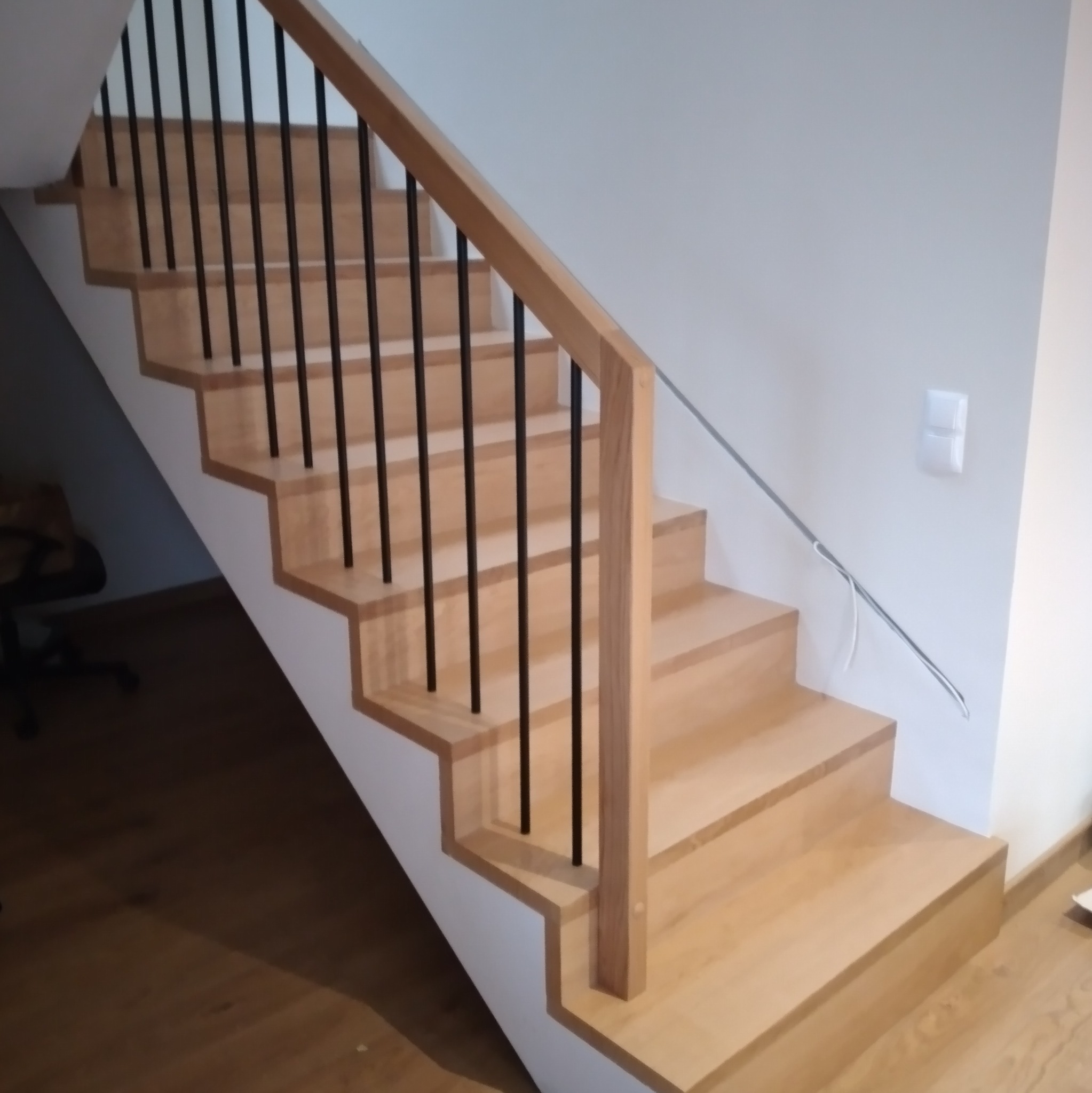 Jasne, drewniane schody z czarnymi, metalowymi balustradami w nowoczesnym domu, widoczne z dołu.