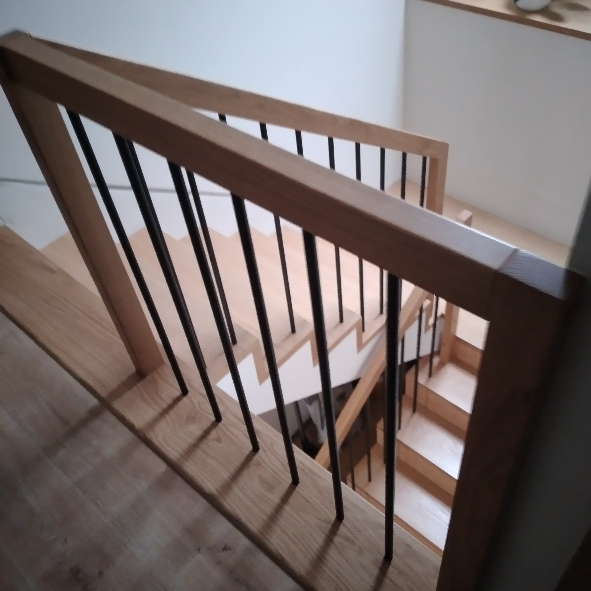 Nowoczesne schody z jasnego drewna z czarnymi, metalowymi tralkami, widok z góry na poręcz.
